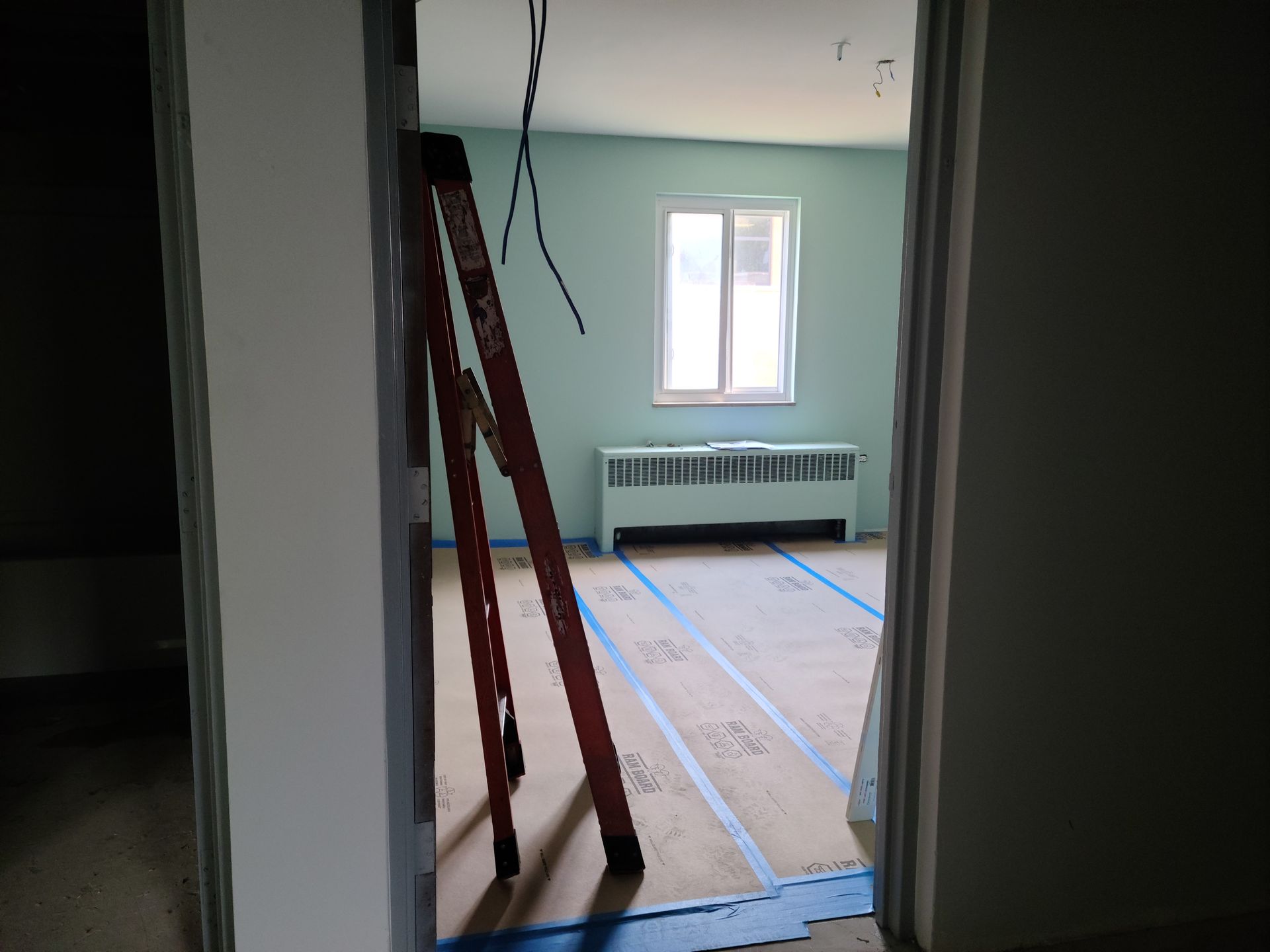 Room under construction with a ladder, pale green walls, and new flooring. View through a doorway.