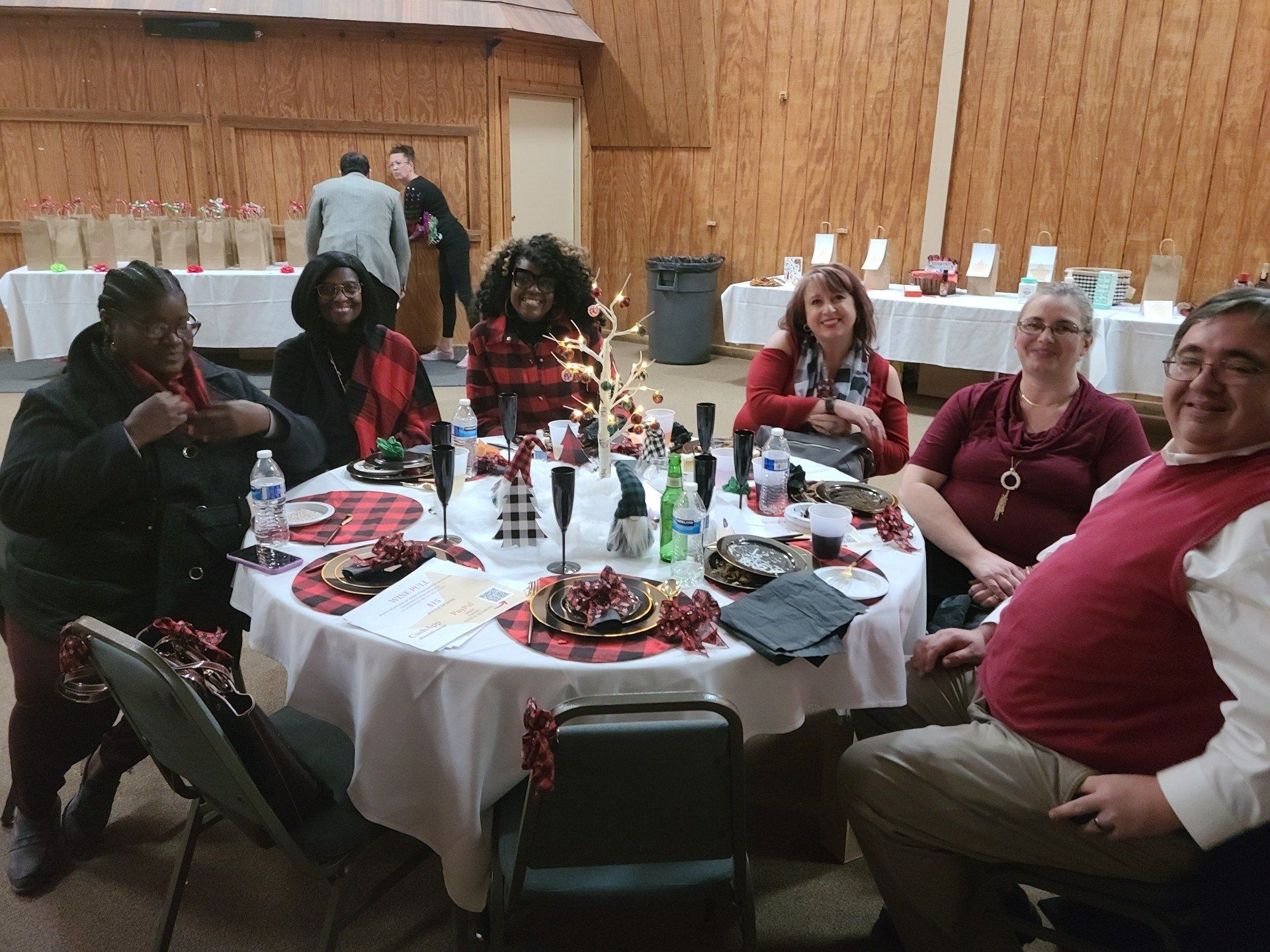 Group of people at a round table, decorated for a holiday event, smiling.