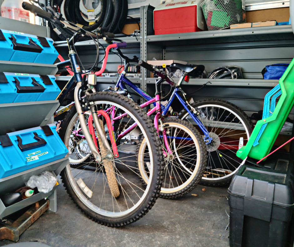 Three bicycles are stored in a cluttered shed next to blue toolboxes.