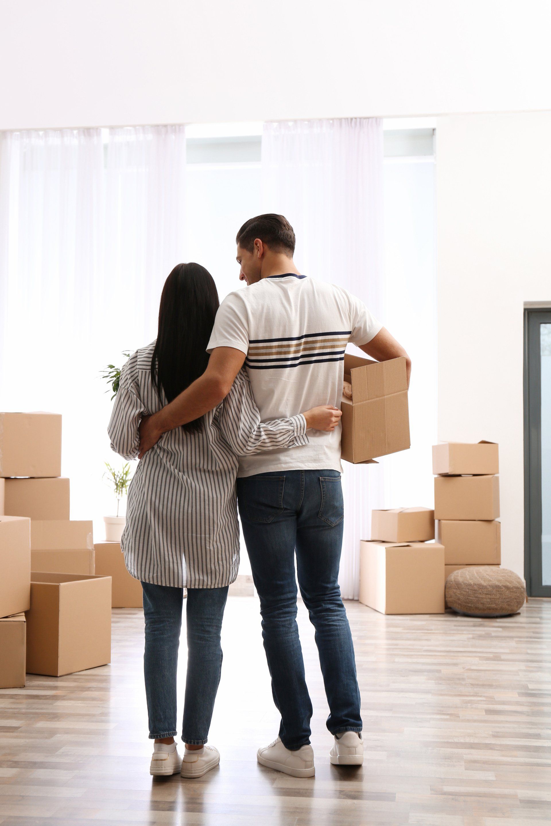 Couple embraces in new home, surrounded by moving boxes.