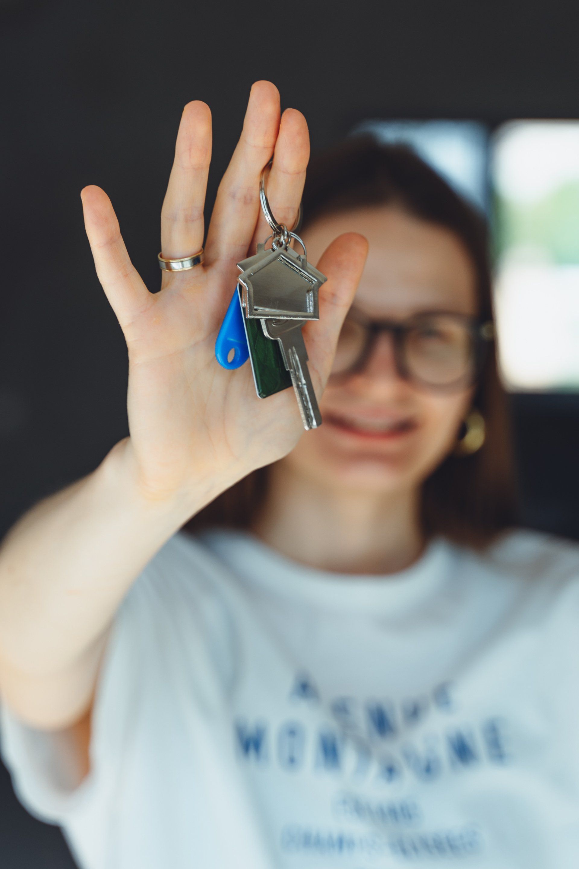 Woman holding out a set of keys with a house-shaped key tag; blurry background.