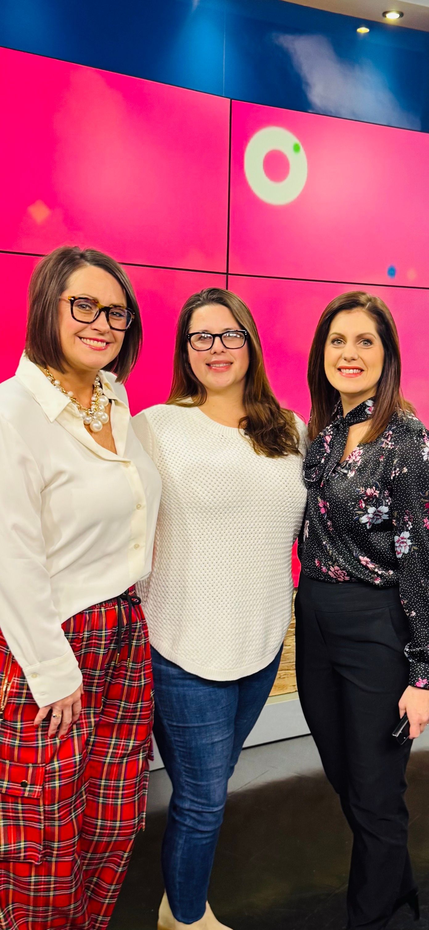 Three women smiling for a photo in front of a pink backdrop.