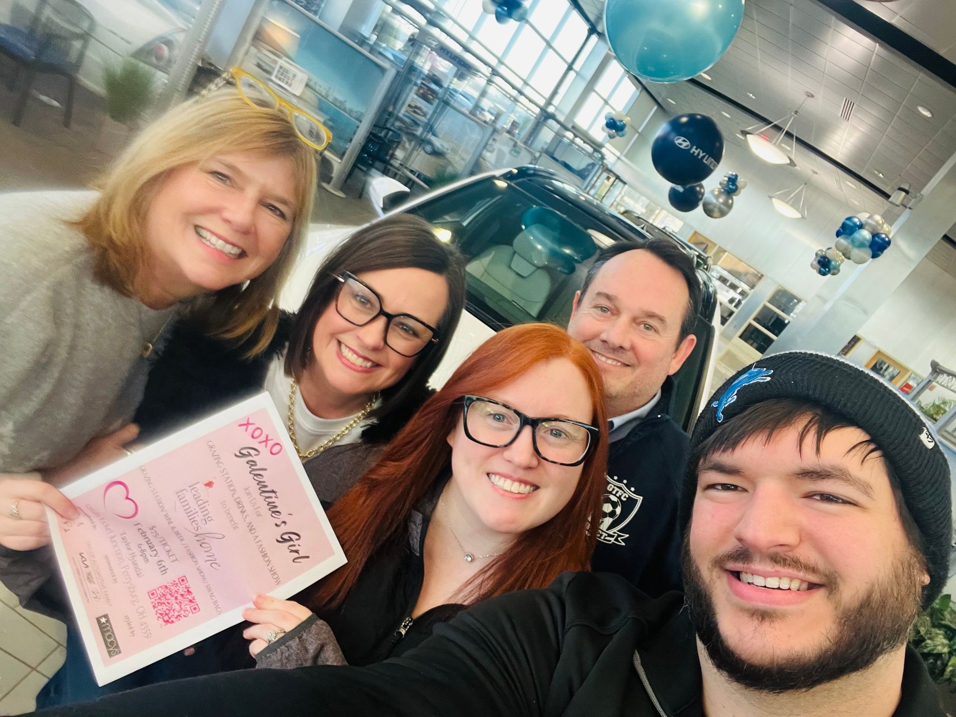 Group of people in a car dealership celebrating, holding a certificate, smiling.