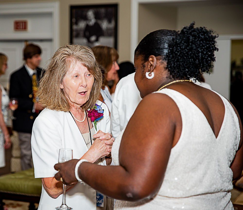 Two women, one white and one Black, converse at an event. The white woman holds a champagne flute.