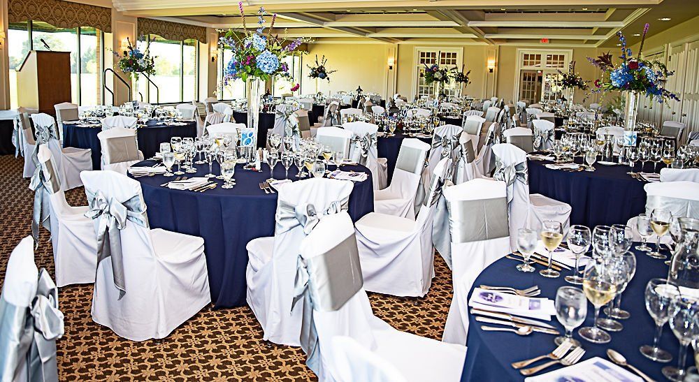 Ballroom set for a wedding with navy tablecloths, white chair covers, and floral centerpieces.