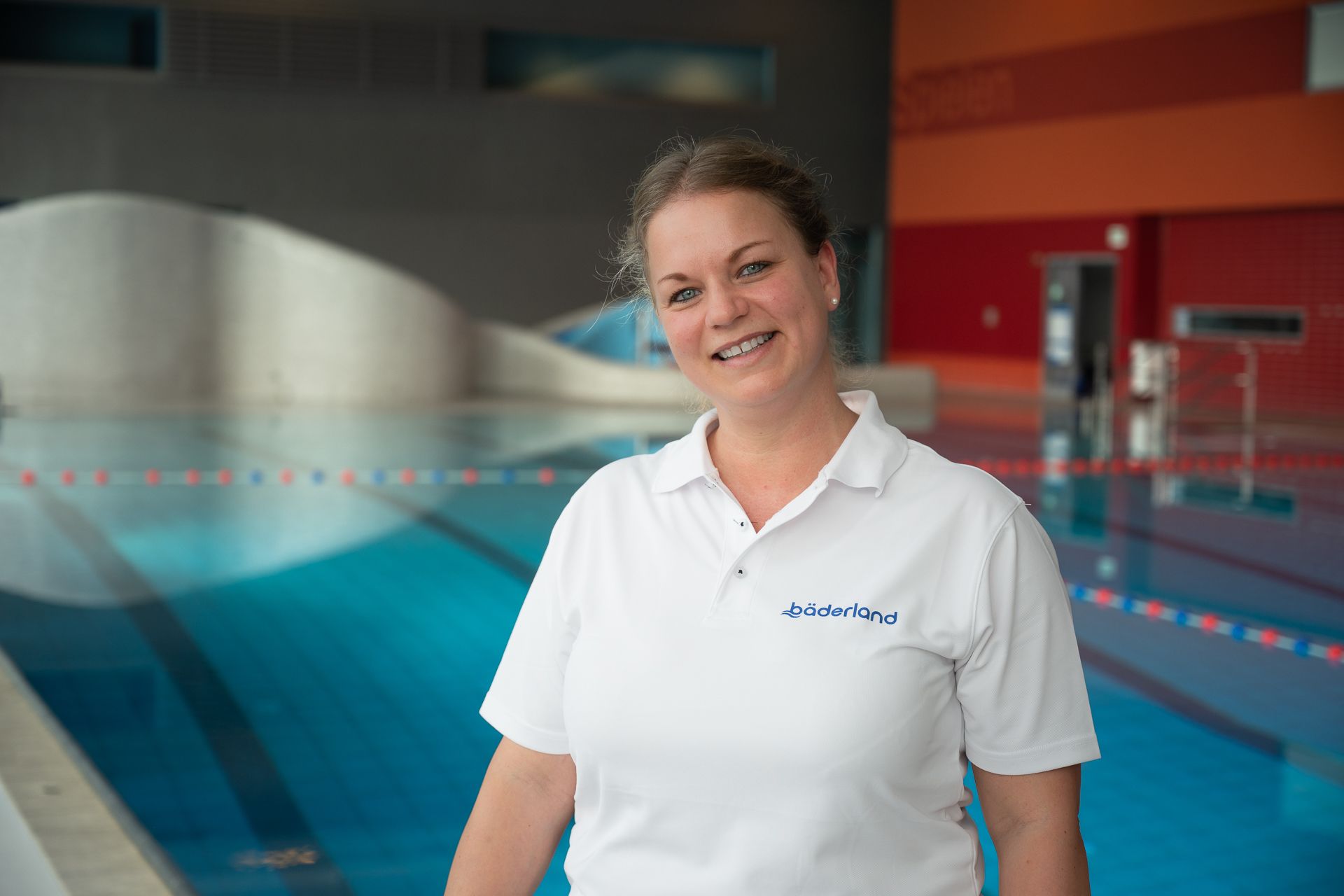 Eine Frau in einem weißen Poloshirt lächelt vor einem blauen Swimmingpool.