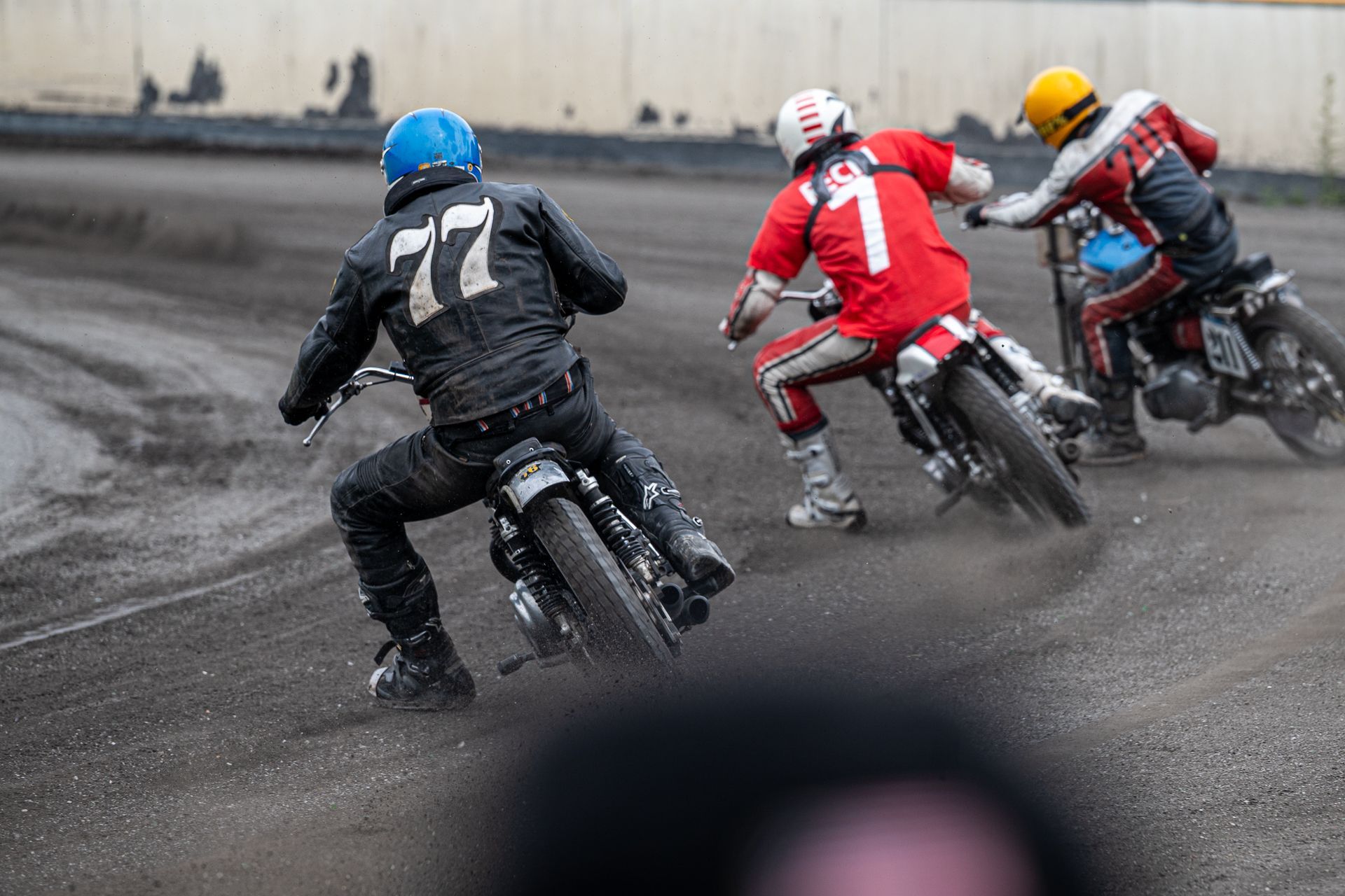 Motorradrennfahrer, Dirt-Track-Rennstrecke, Kurvenfahrt. Fahrer in Schwarz, Nr. 77, rot und gelb. Staub.