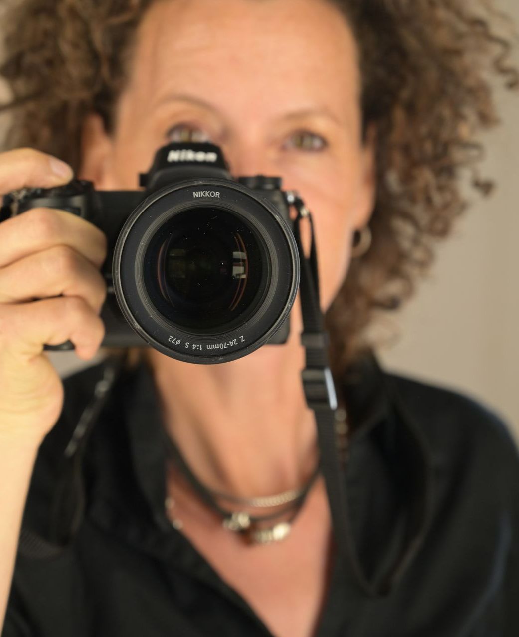Frau hält eine Nikon-Kamera und macht ein Foto. Nahaufnahme zeigt das Kameraobjektiv.