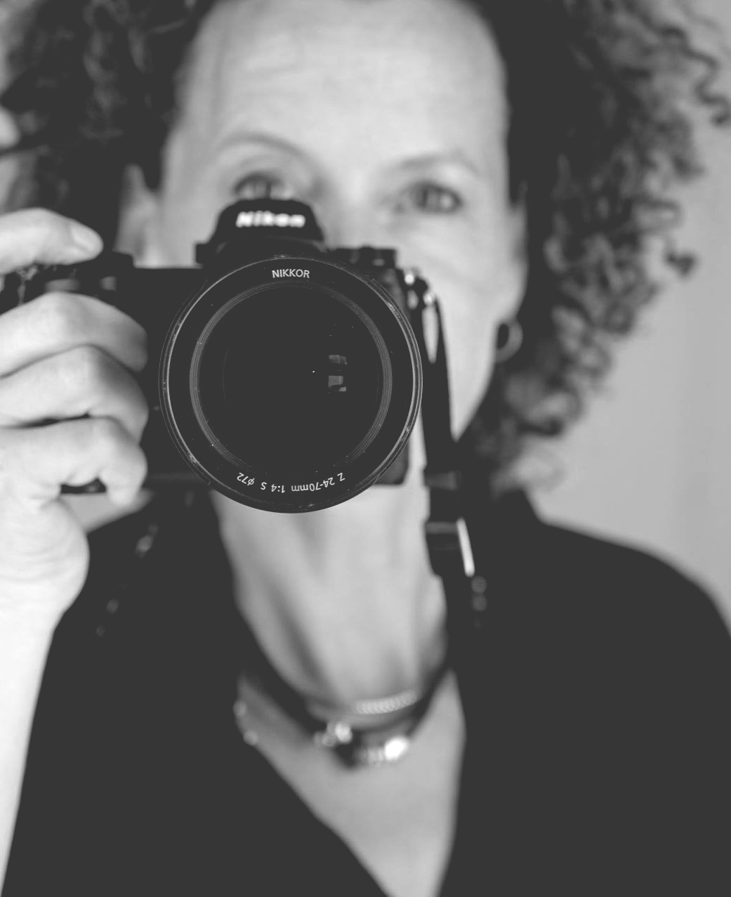 Frau hält eine Nikon-Kamera und macht ein Foto. Nahaufnahme zeigt das Kameraobjektiv.