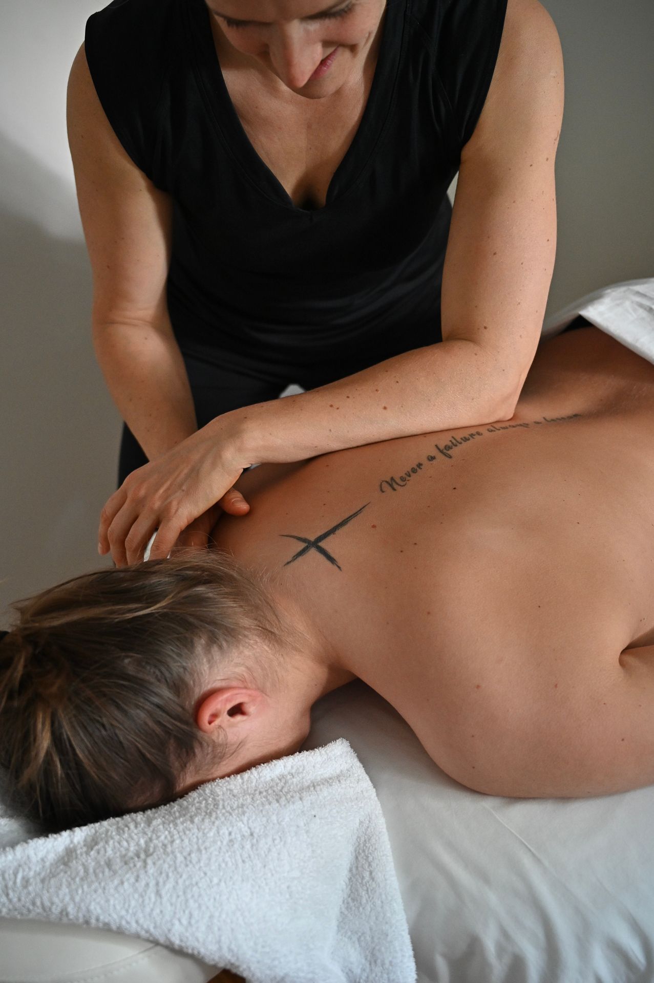 Eine Person erhält eine Rückenmassage auf einem weißen Handtuch. Eine Person in schwarzer Kleidung massiert den oberen Rücken der anderen.