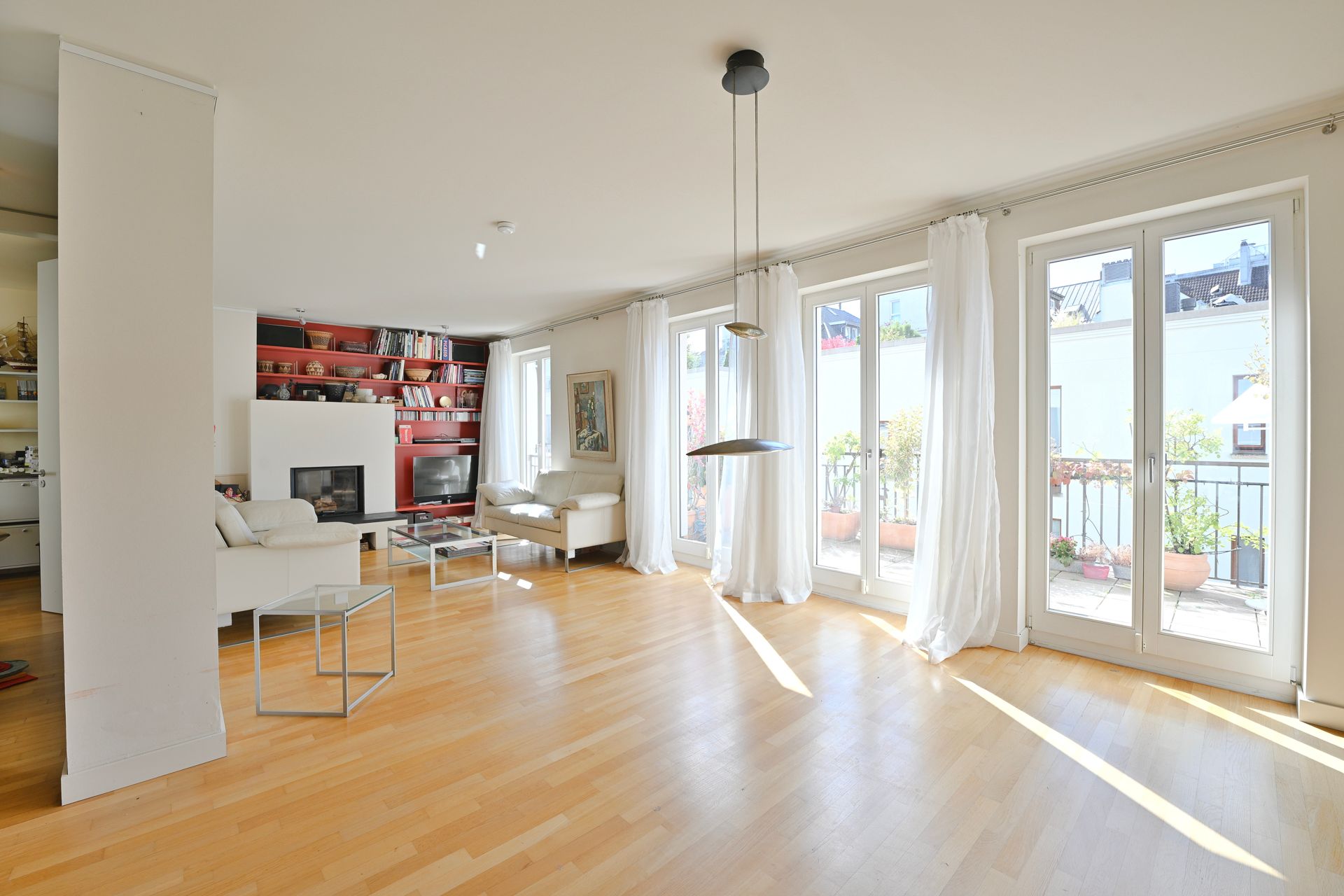Helles, luftiges Wohnzimmer mit Holzboden, weißen Möbeln, Kamin und Zugang zum Balkon.