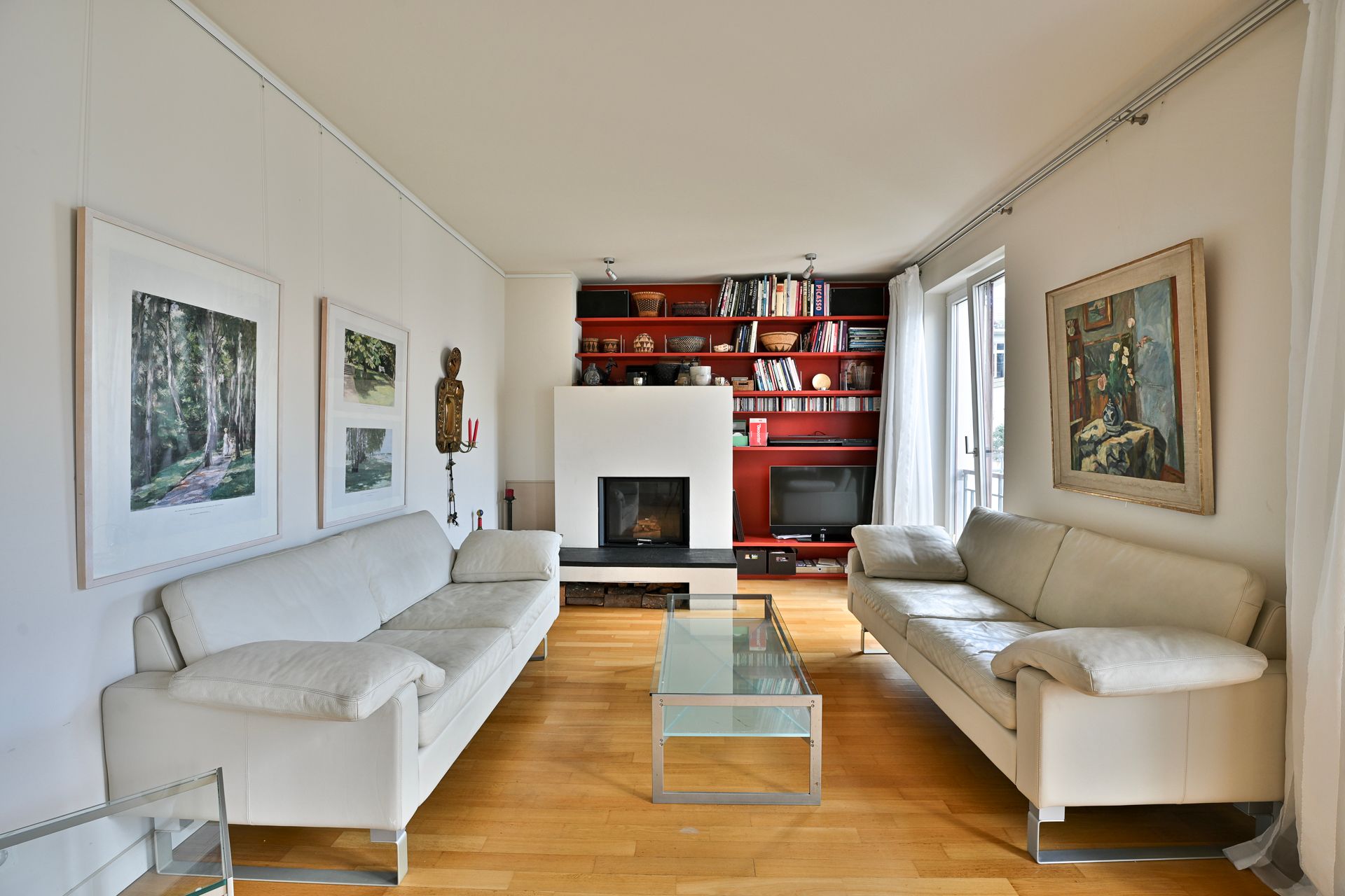 Wohnzimmer mit weißen Sofas, Kamin, Bücherregalen und Kunstwerken.