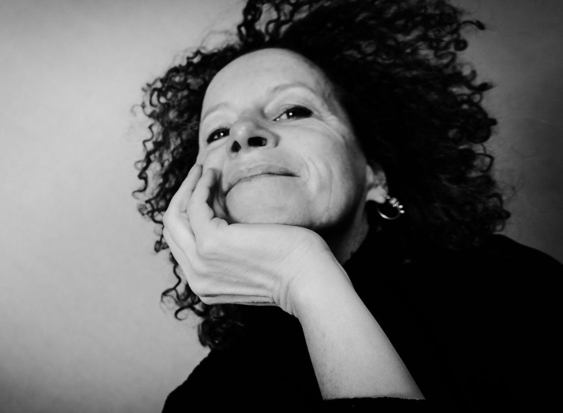 Frau mit lockigem Haar, die Hand am Kinn, blickt nachdenklich nach oben.