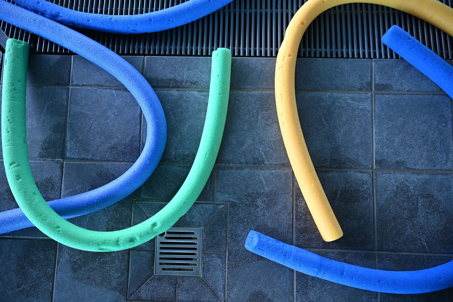 Bunte Poolnudeln auf einer dunklen Fliesenfläche mit Abfluss.