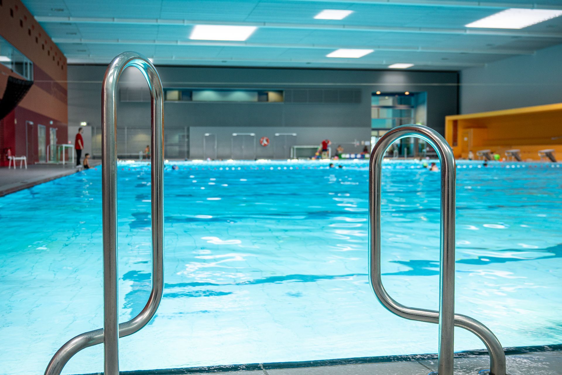 Hallenbad mit Personen im Wasser. Edelstahlgeländer im Vordergrund.