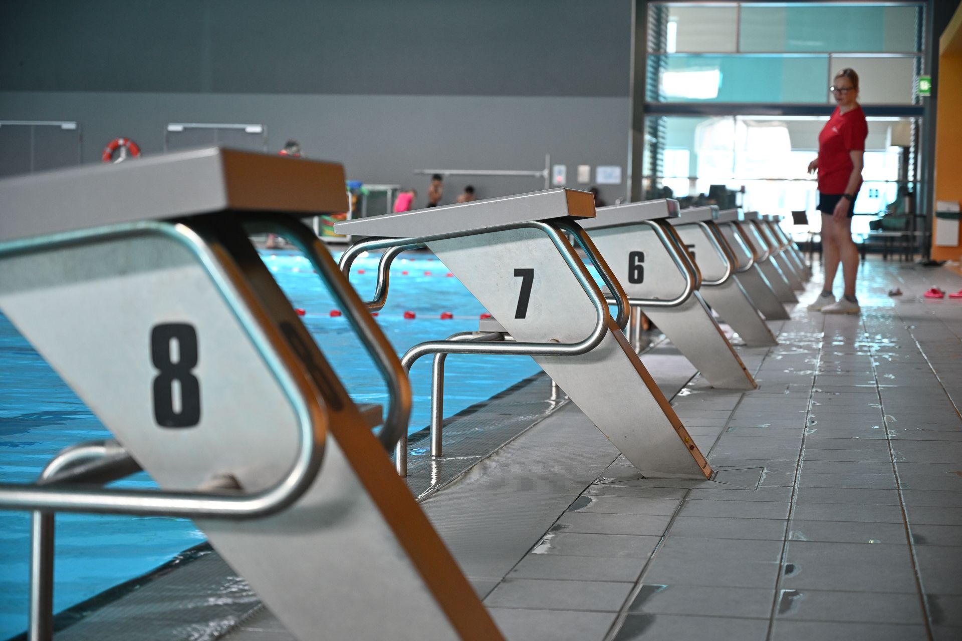 Startblöcke im Pool, nummeriert 8, 7, 6 usw. Eine Person im roten Hemd steht in der Nähe.