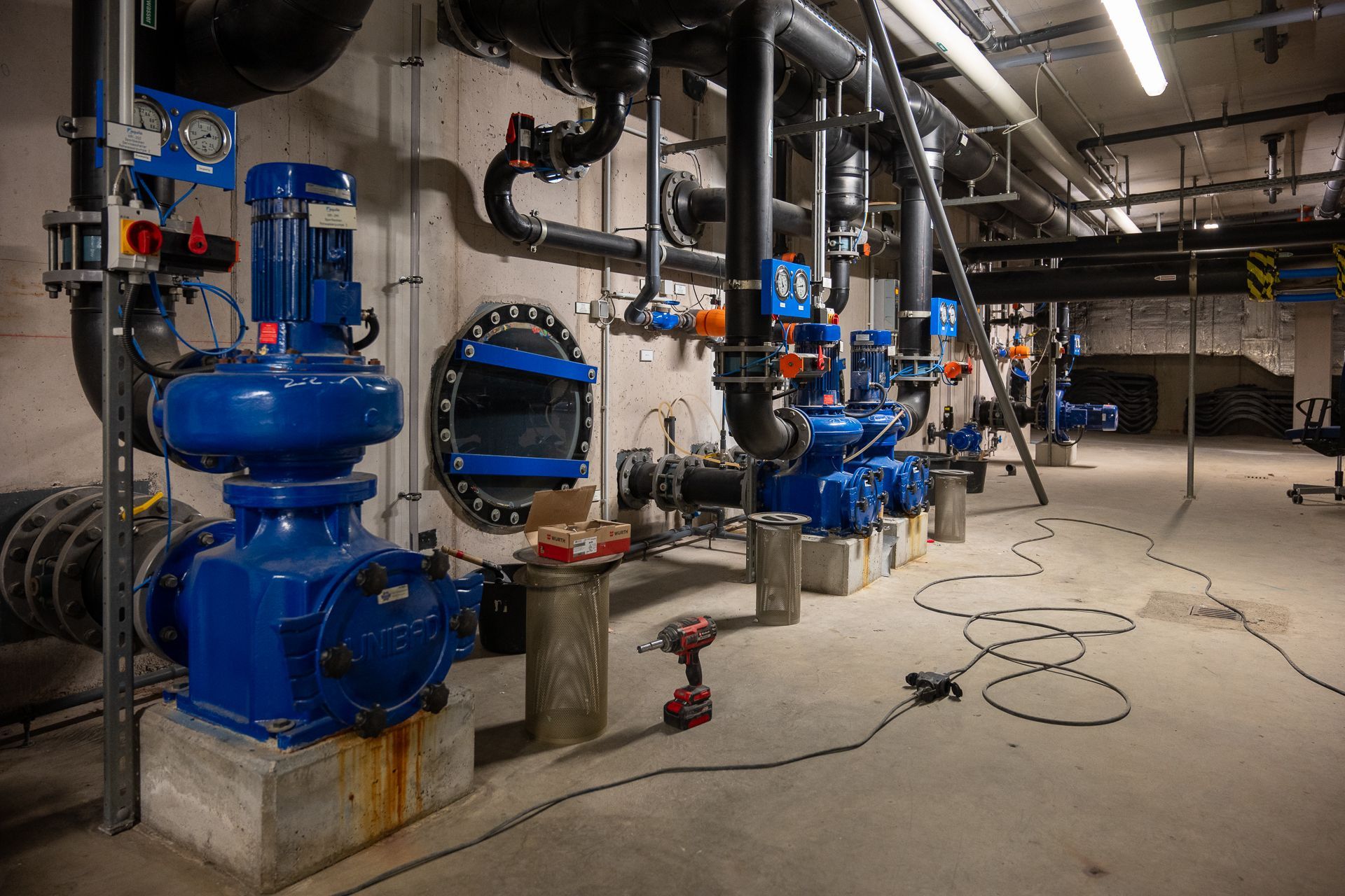Blaue Industriepumpen und -rohre in einem Betonraum mit Werkzeugen deuten auf eine Wasseraufbereitungsanlage oder Ähnliches hin.