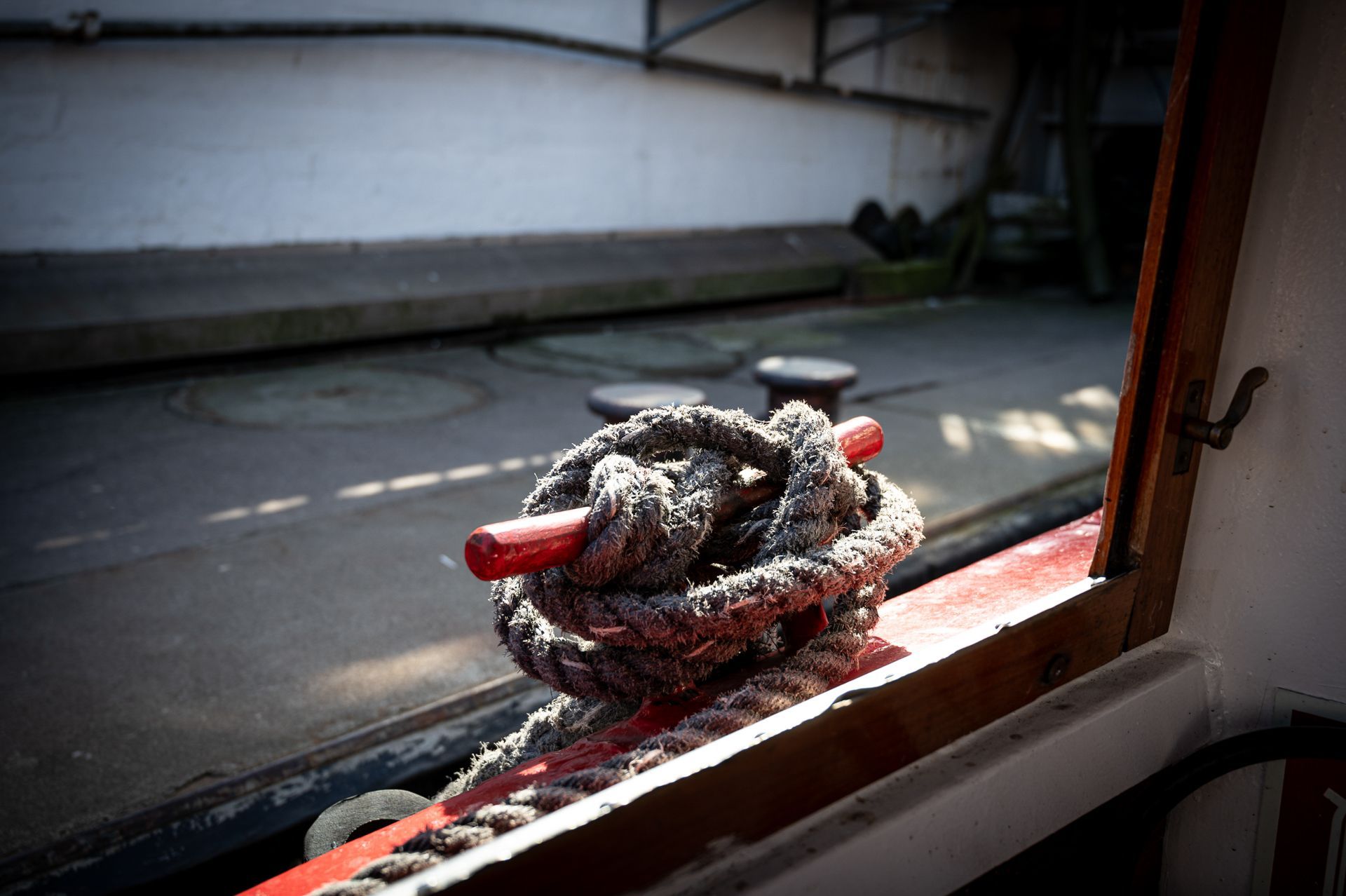 Ein um eine rote Klampe an einem Boot gewickeltes Seil wirft einen Schatten im Hafen.