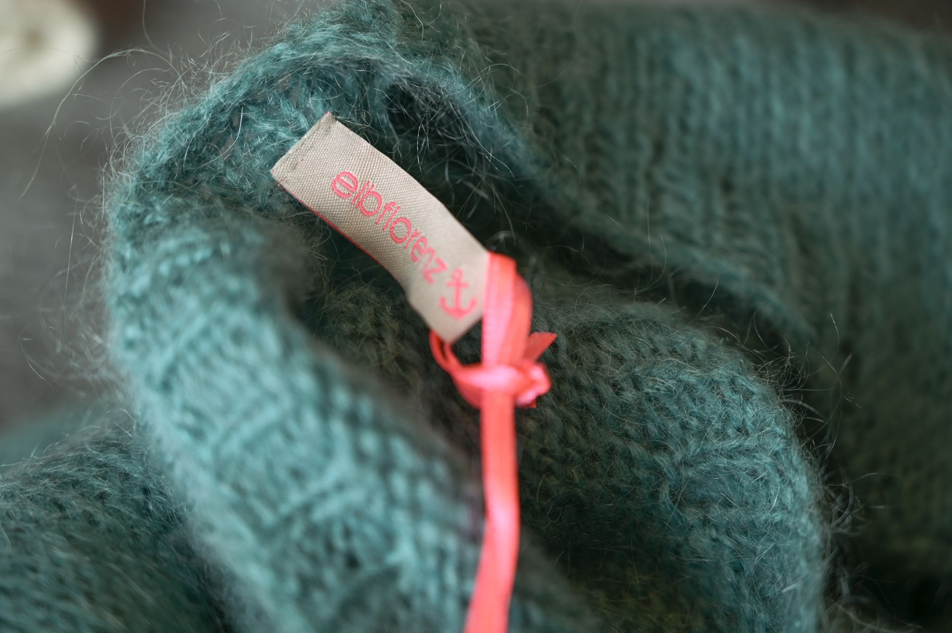 Nahaufnahme eines türkisfarbenen Strickkleidungsstücks, an dem ein Etikett mit einer rosa Schnur befestigt ist.