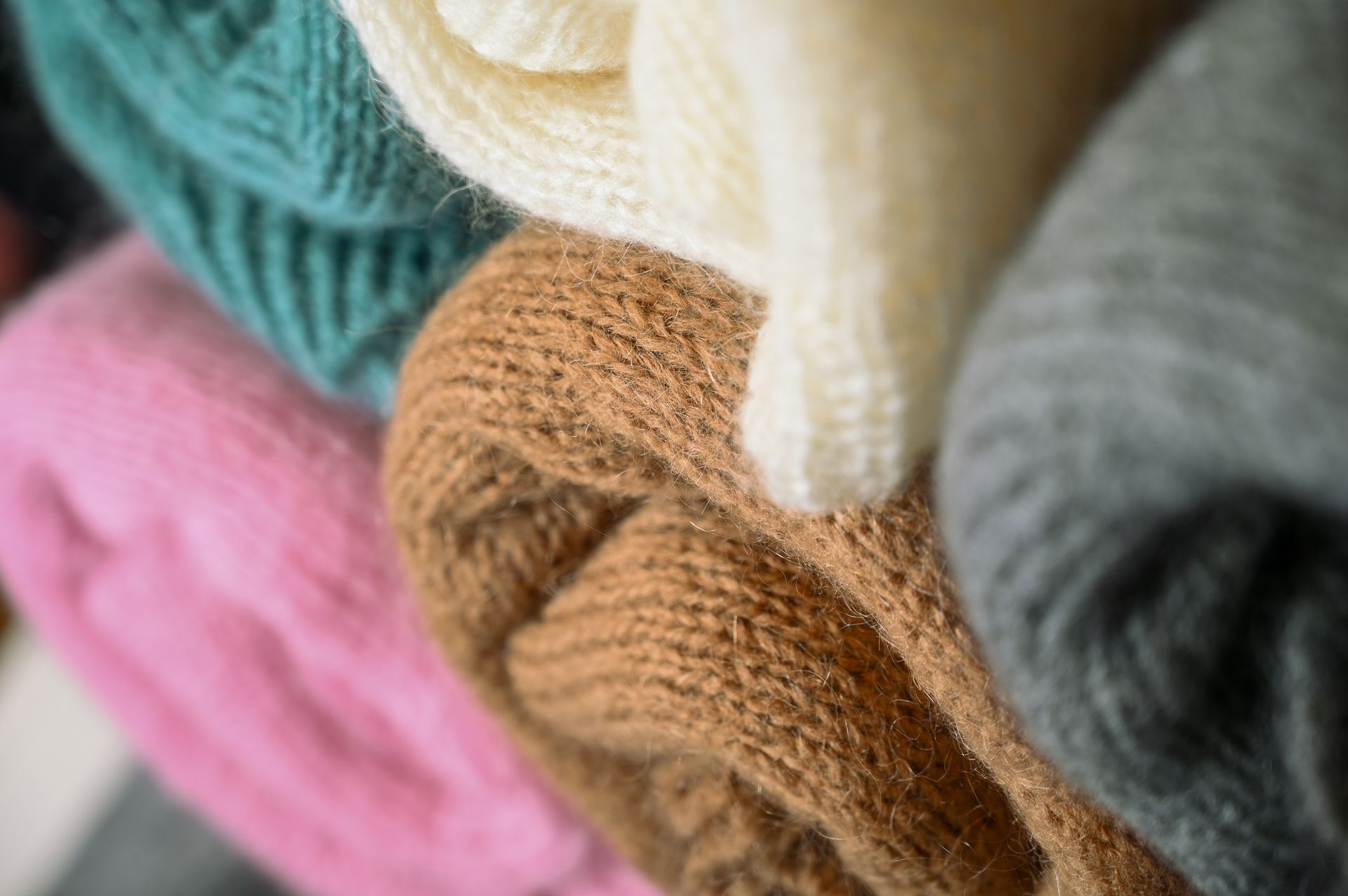 Zusammengerollte Strickwaren in verschiedenen Farben: Türkis, Creme, Braun, Rosa und Grau.