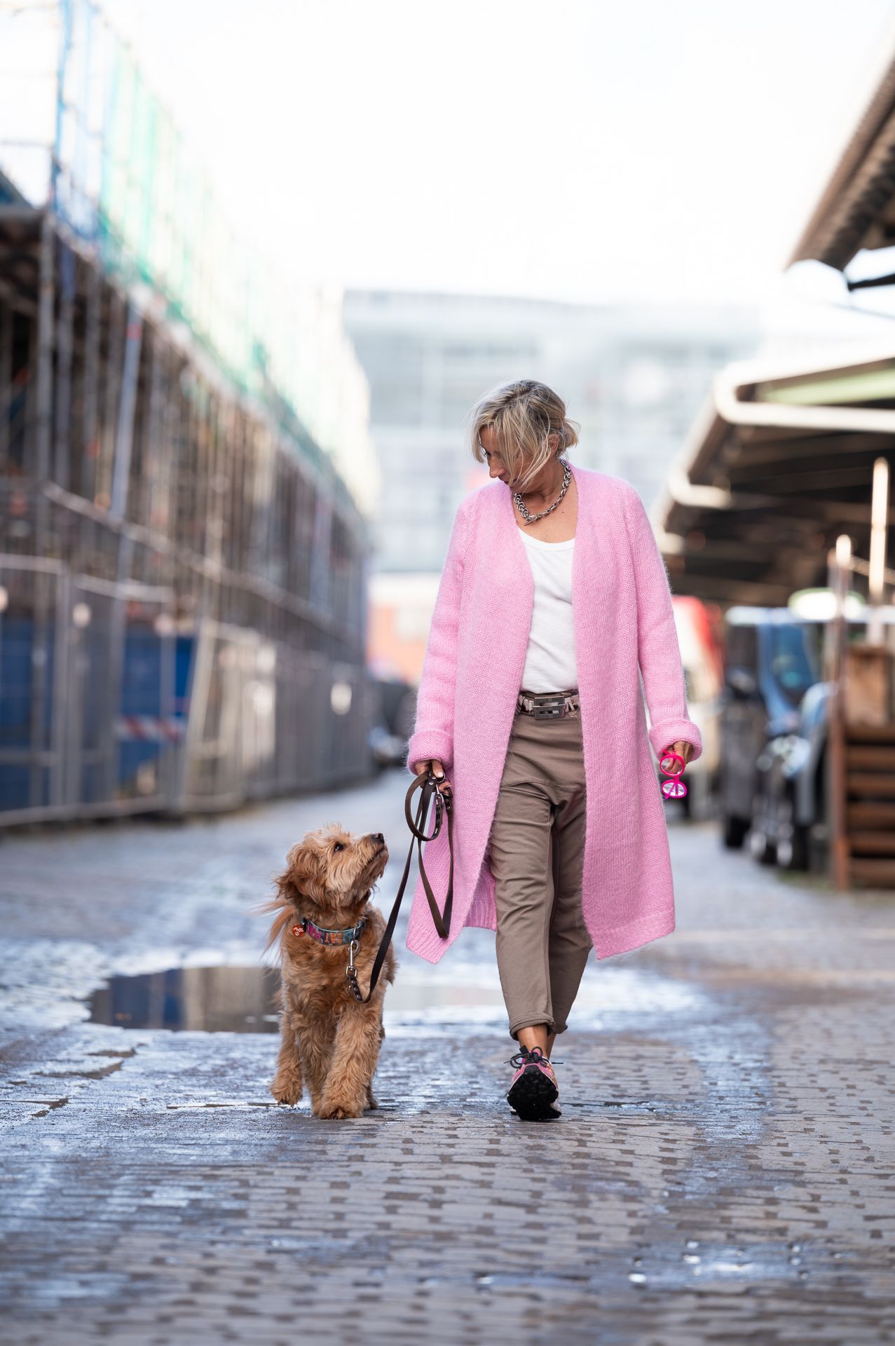 Frau in rosa Mantel führt Hund an der Leine, städtische Umgebung.