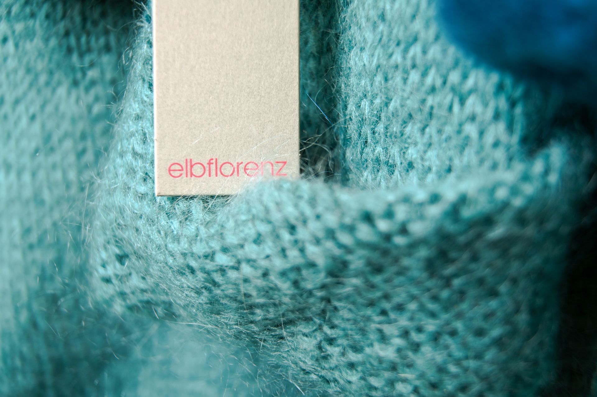Etikett mit dem „ebflorenz“-Logo auf türkisfarbener Strickware.