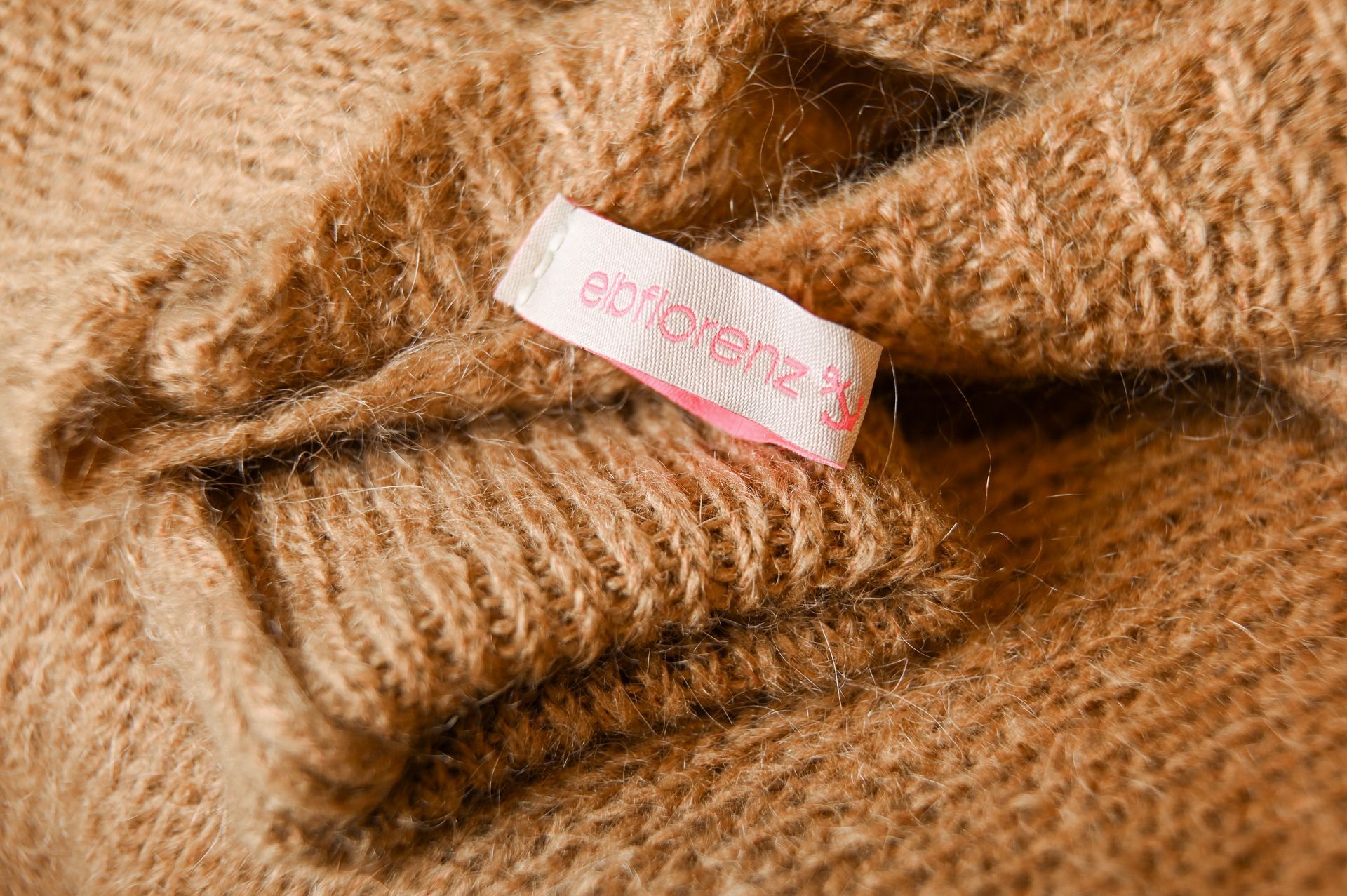 Hellbrauner Strickpullover mit einem rosa-weißen Etikett.