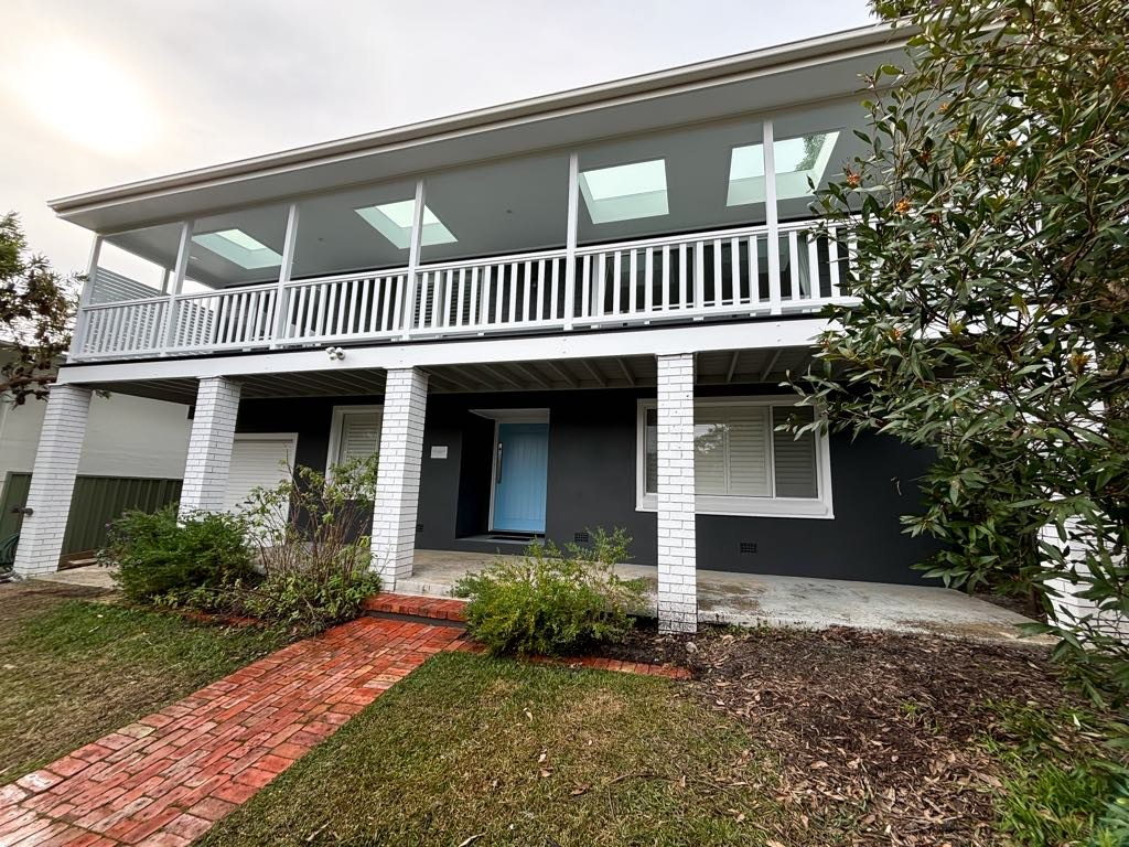 Two-story house with white balcony railings, brick walkway, and front porch surrounded by greenery