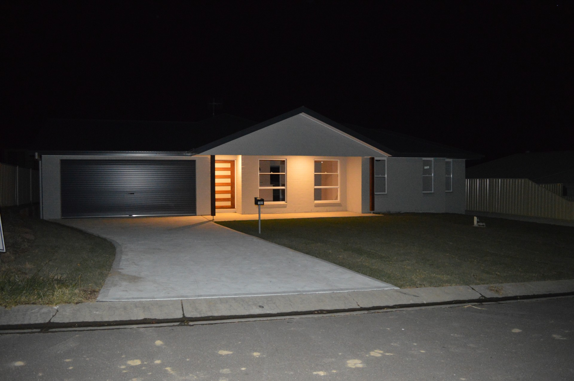 Single-story house at night with porch light on, driveway and garage visible.