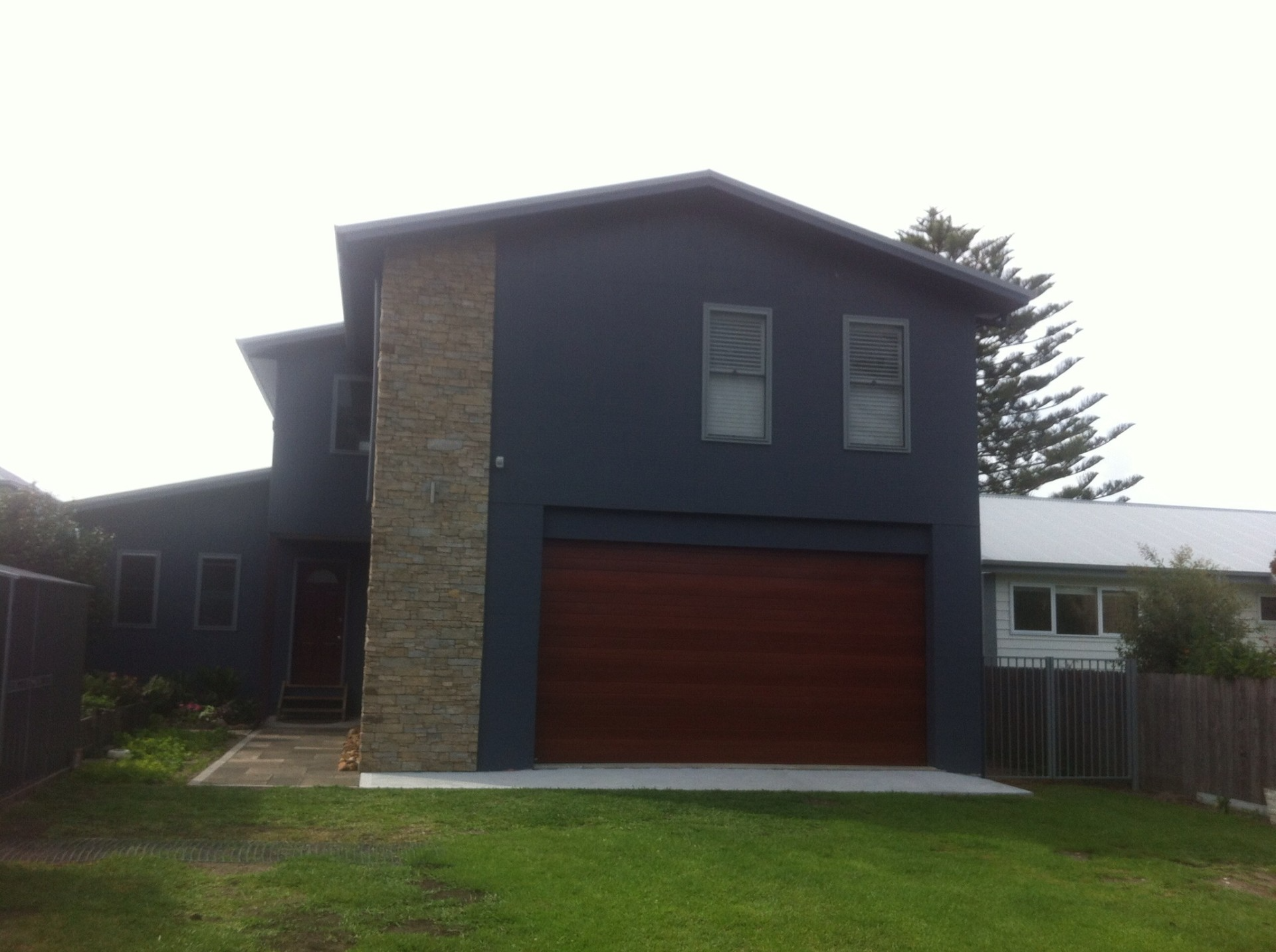 Modern two-story house with dark siding, wood garage door, and green lawn