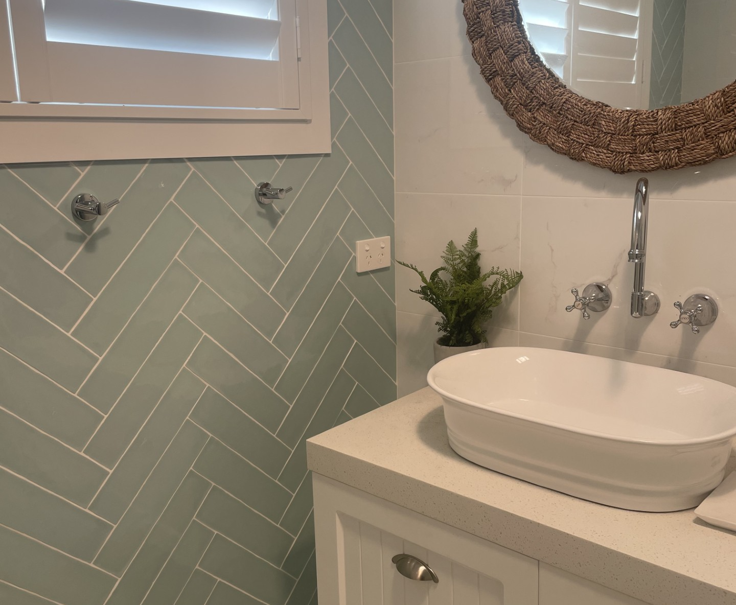 Bathroom with pale green herringbone tile shower, white vanity, vessel sink, and round mirror