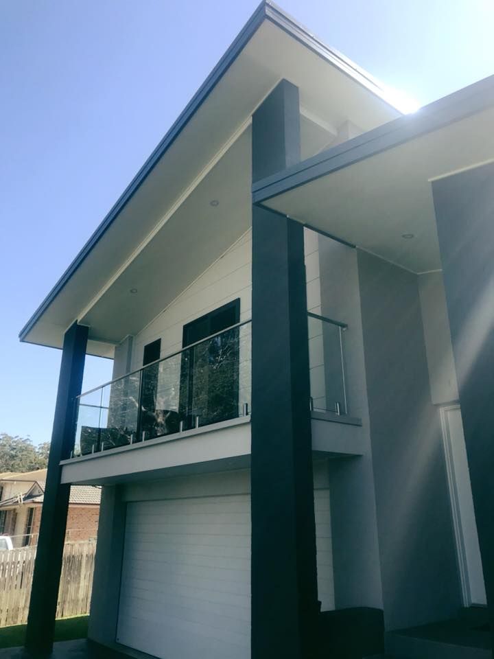 Modern two-story house with balcony, white exterior, and roller garage door under a clear blue sky
