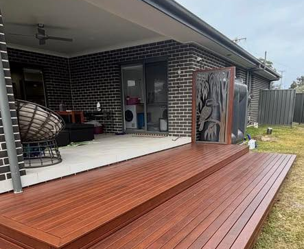 Backyard deck with a wooden platform, covered patio, and decorative screen beside a brick house.