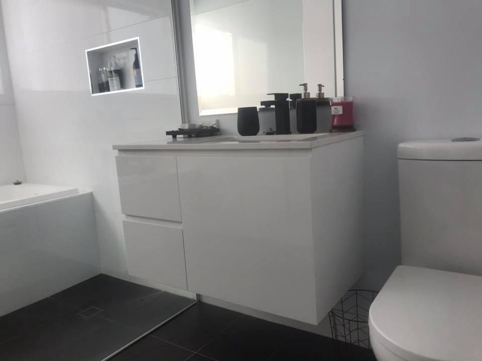 Small bathroom with white vanity, sink, and toilet beside a black-tiled shower floor.