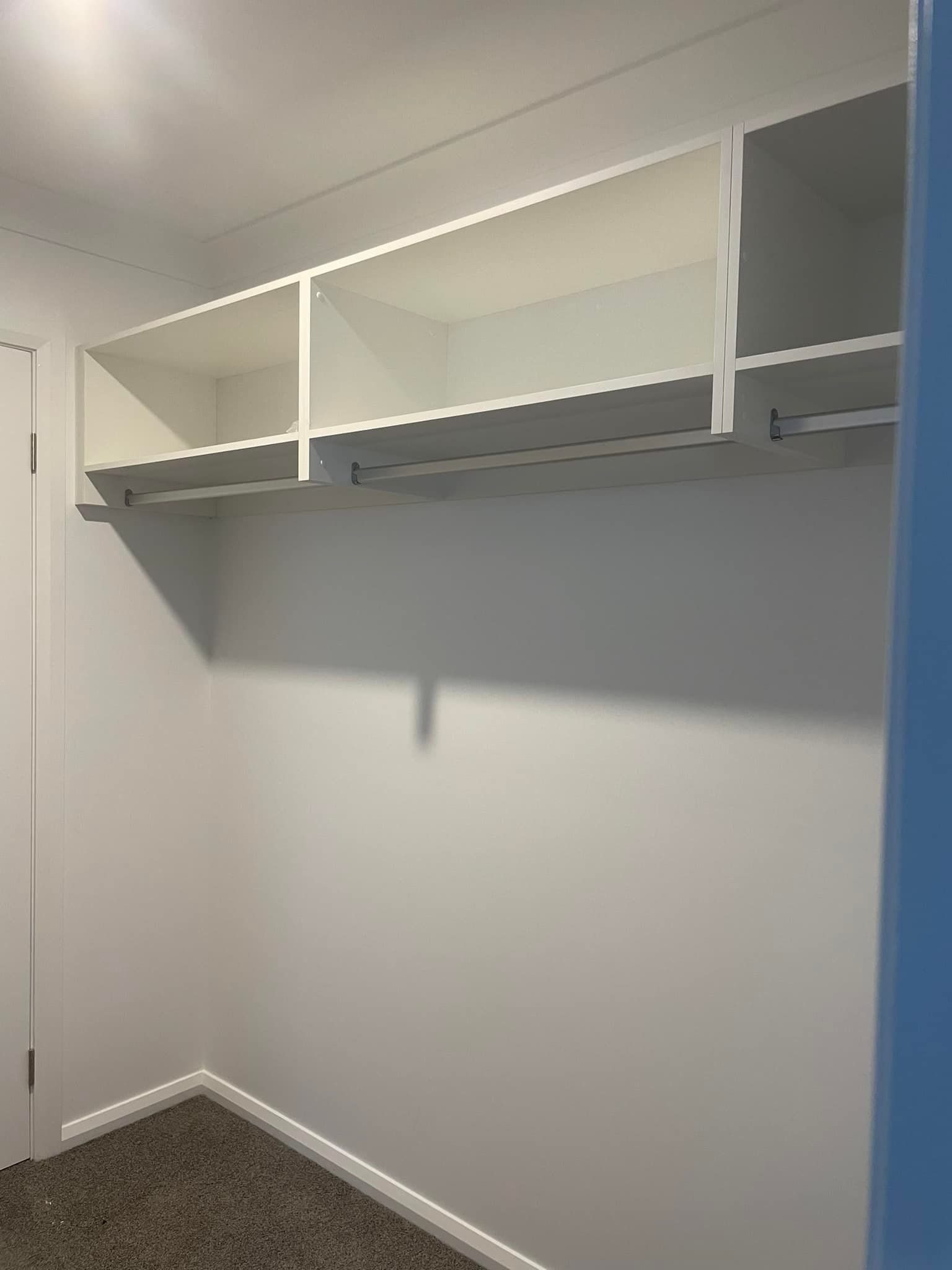 Empty walk-in closet with white shelves, gray walls, and carpeted floor.