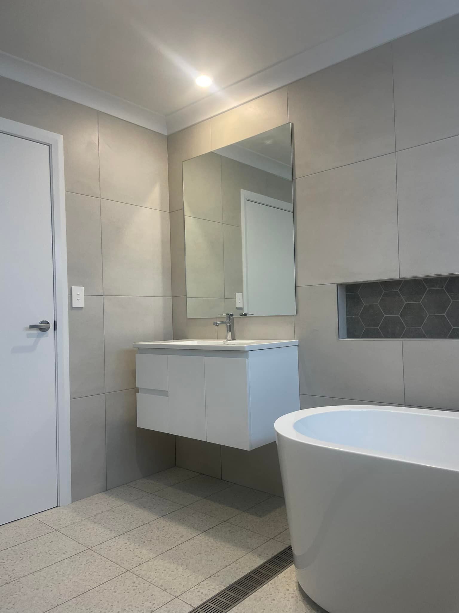Modern tiled bathroom with floating vanity, mirror, and freestanding bathtub