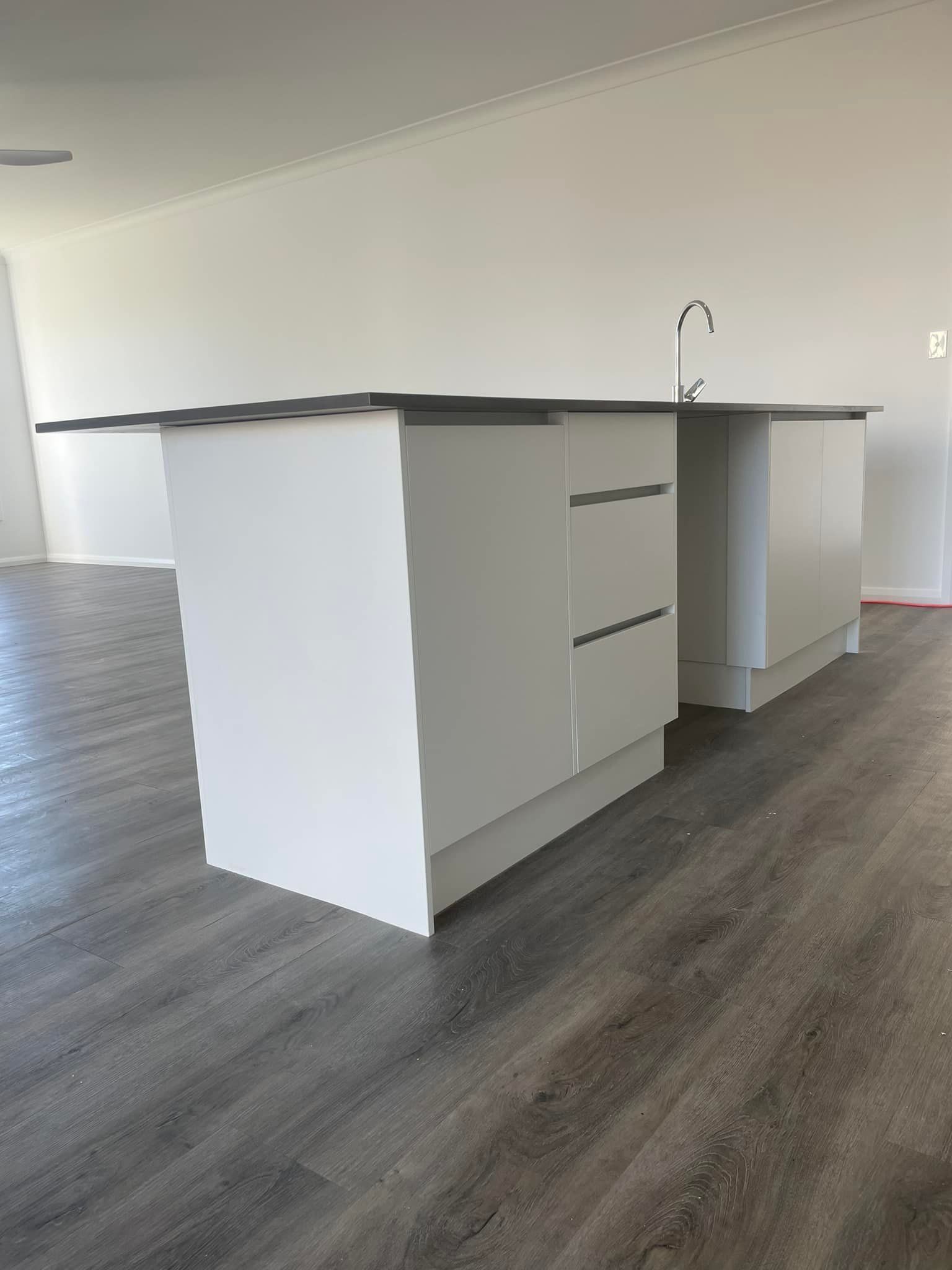 Empty modern kitchen with white island cabinets, sink, and dark wood flooring.