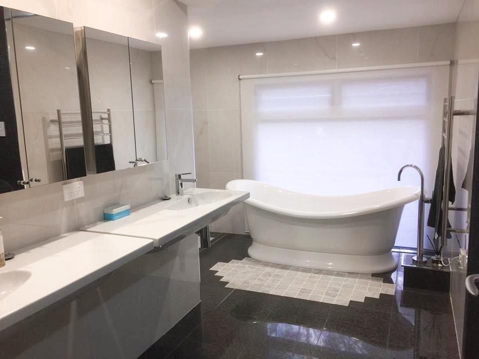 Modern bathroom with double vanity, large mirrors, and a freestanding bathtub by a window.