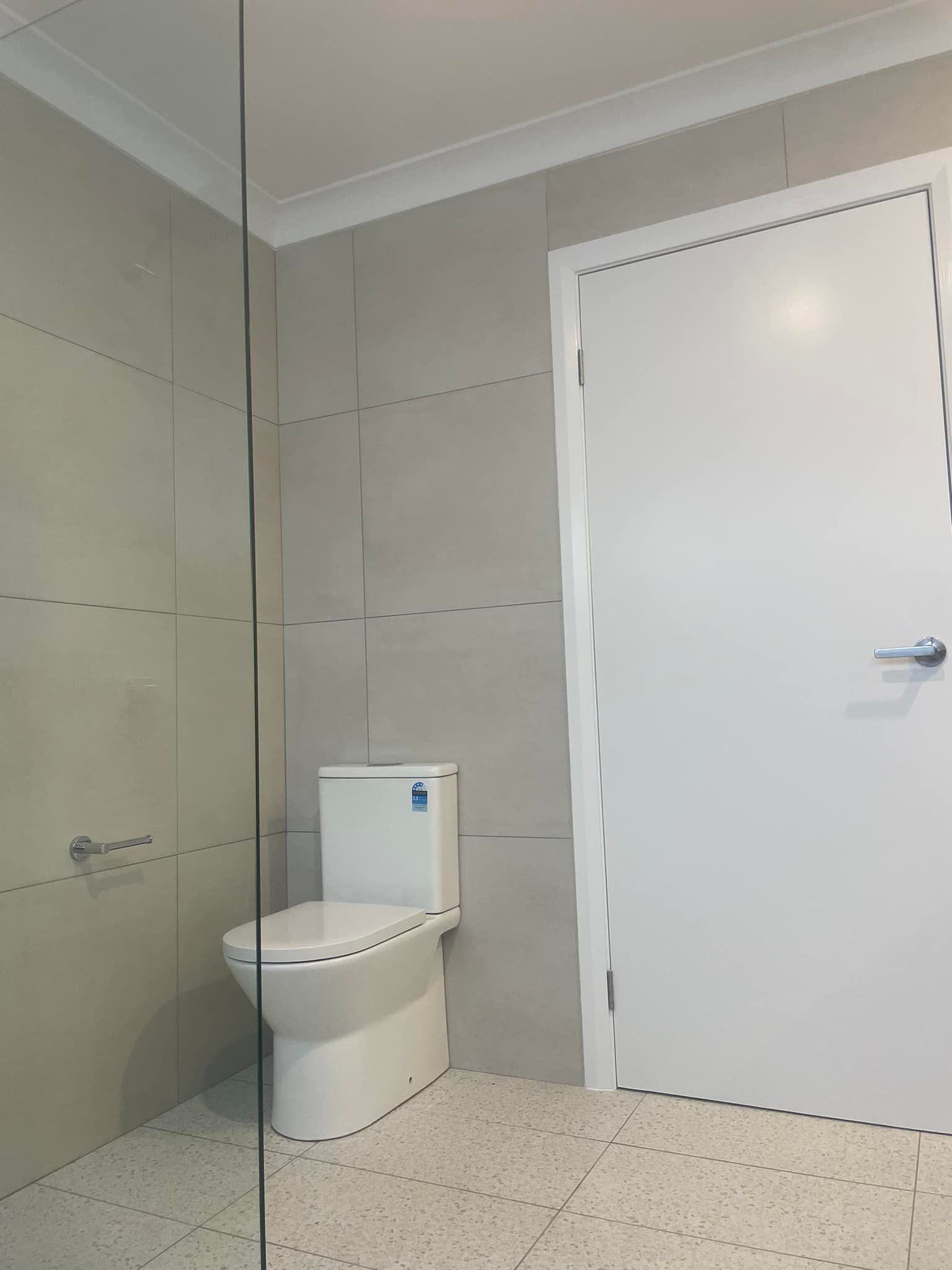 Modern tiled bathroom with a toilet, wall mirror, and white door