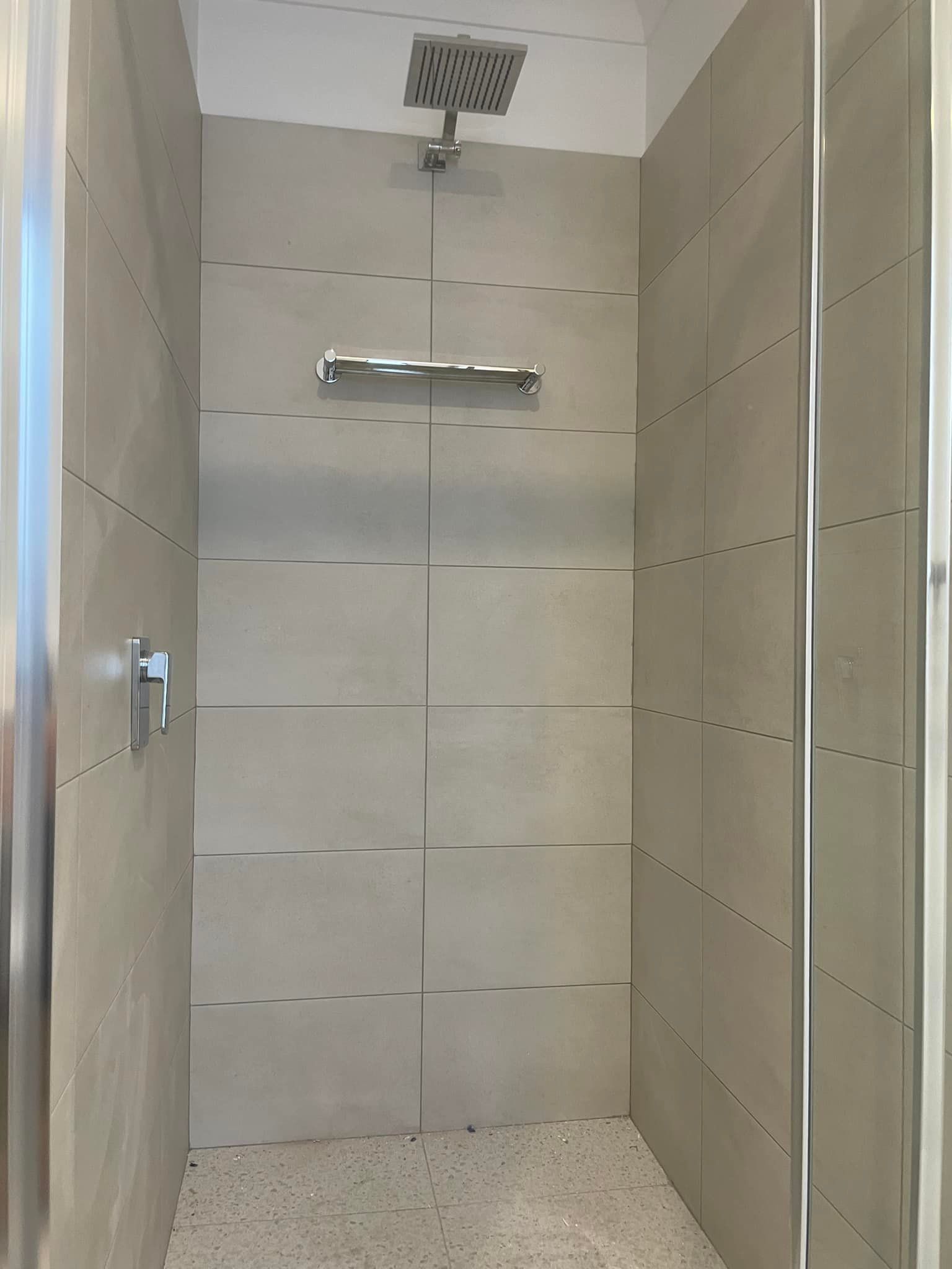 Empty tiled shower stall with chrome showerhead and shelf, viewed through a doorway.