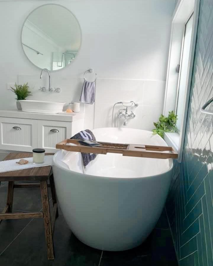Bright bathroom with freestanding tub, white vanity, round mirror, and teal tile accents
