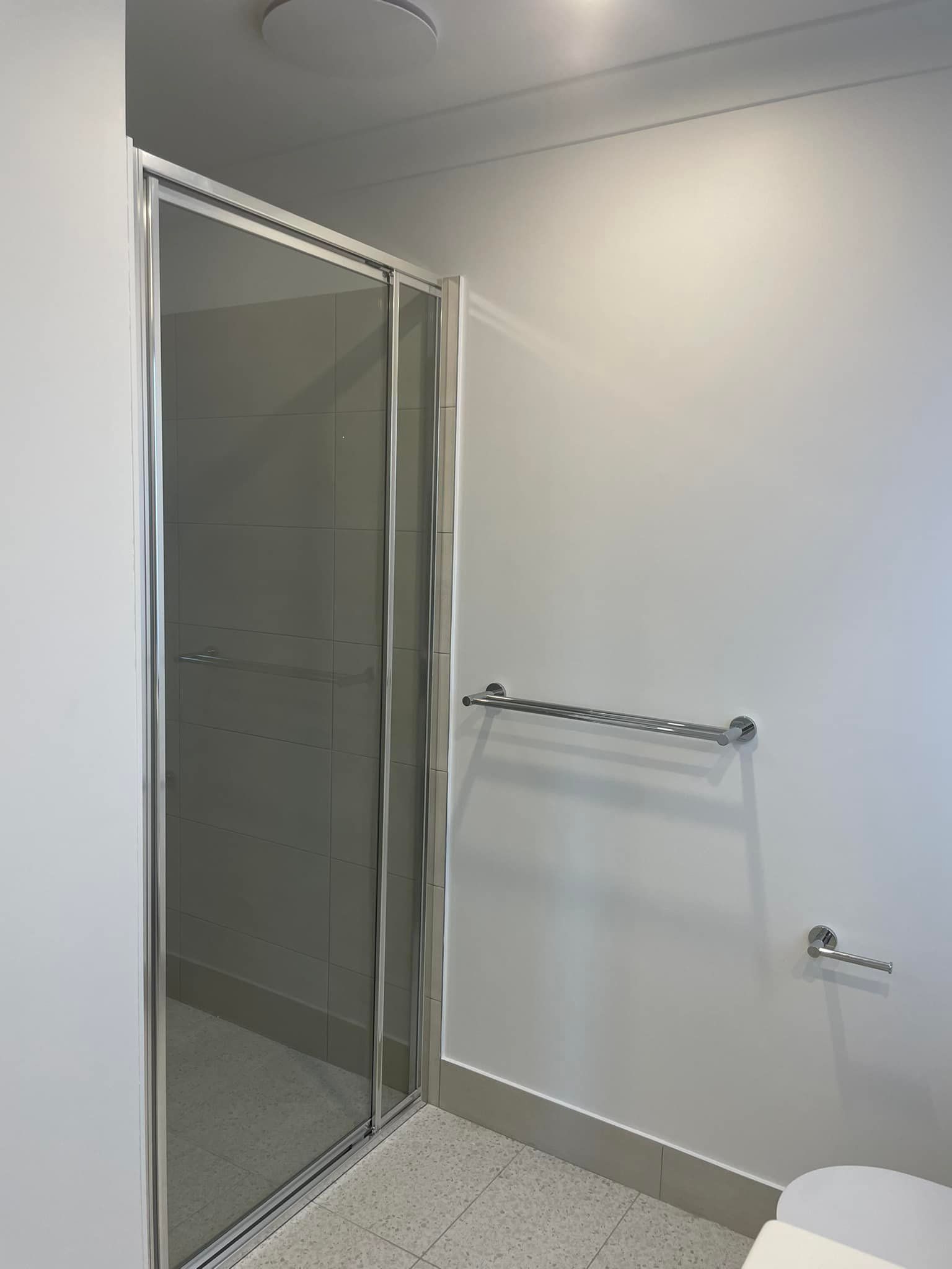 Empty white bathroom with a glass shower, towel rack, and tiled floor.