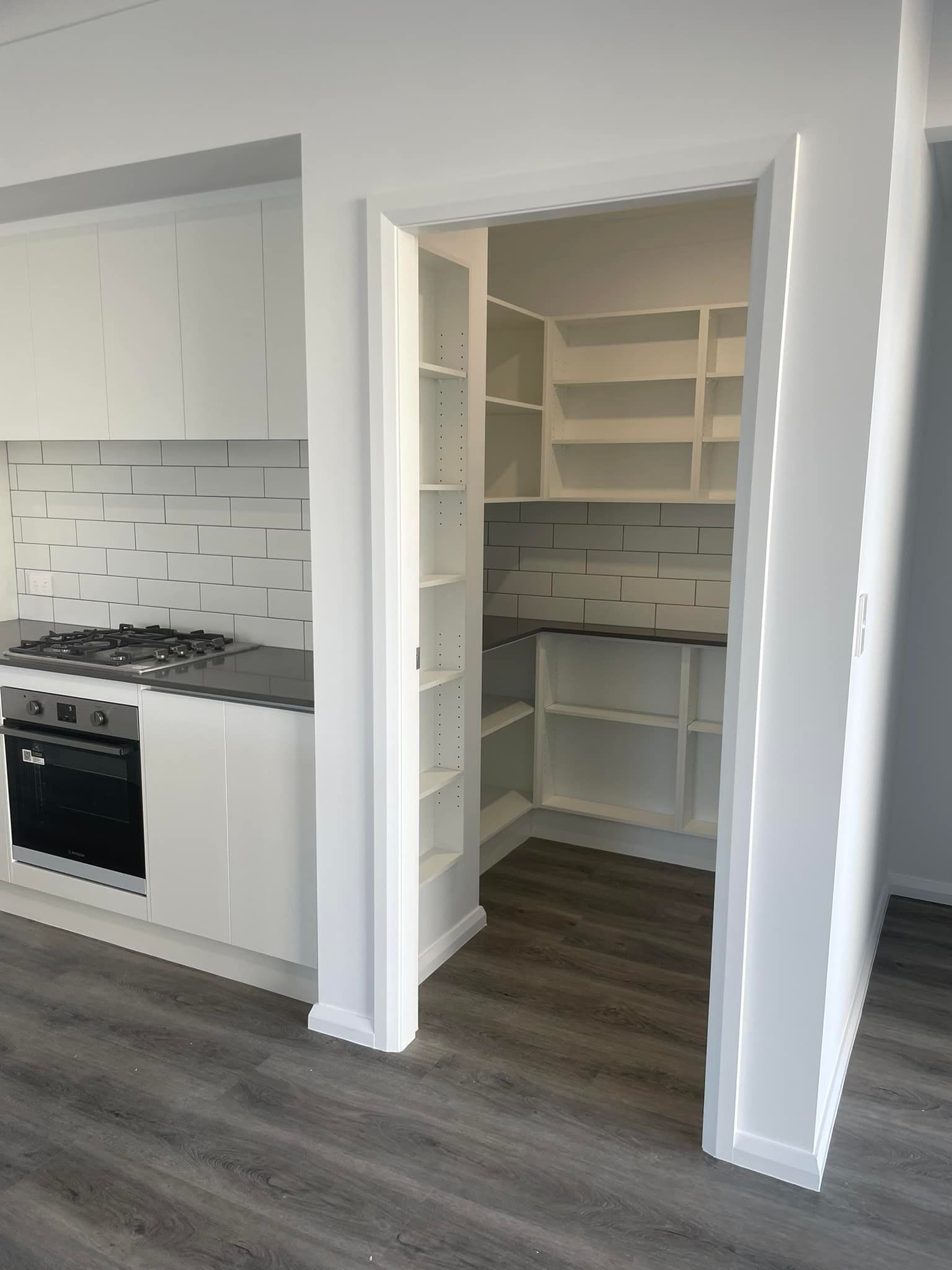 Kitchen with white cabinets, gas stove, and open pantry closet with shelving.