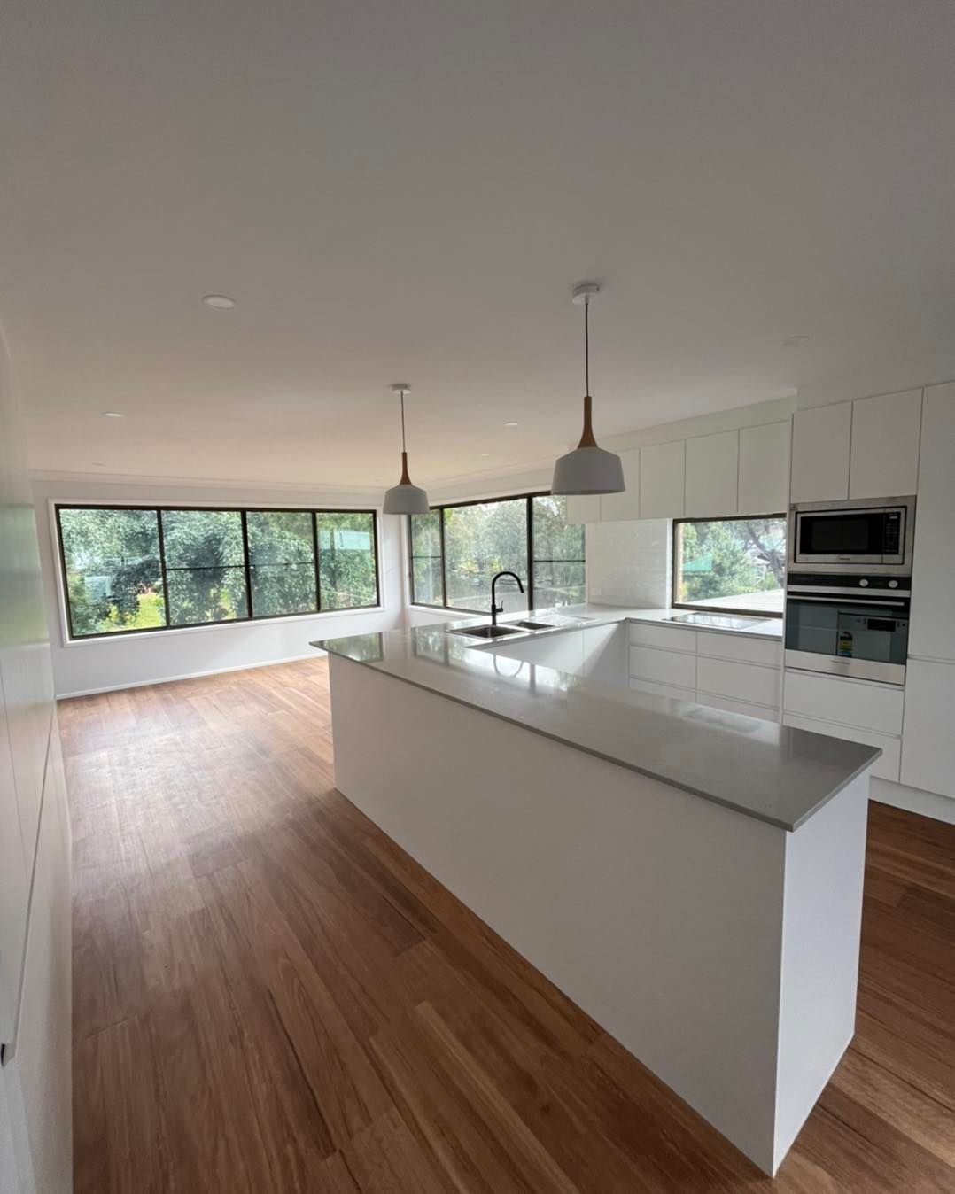 Modern kitchen with white island, wood floors, large windows, and pendant lights
