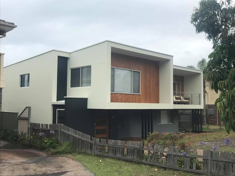 Modern two-story white house with wood accents and a fenced front yard under an overcast sky