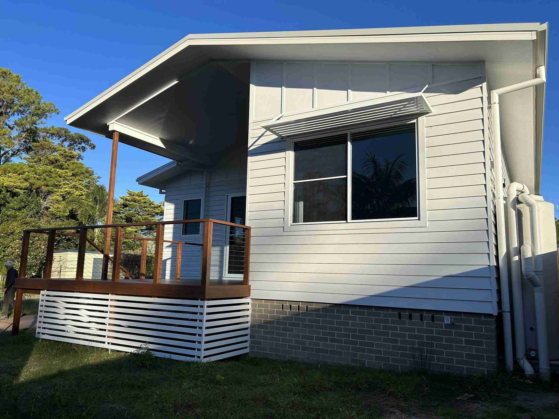 Small white house with a porch, wooden railing, and large front window in sunlight