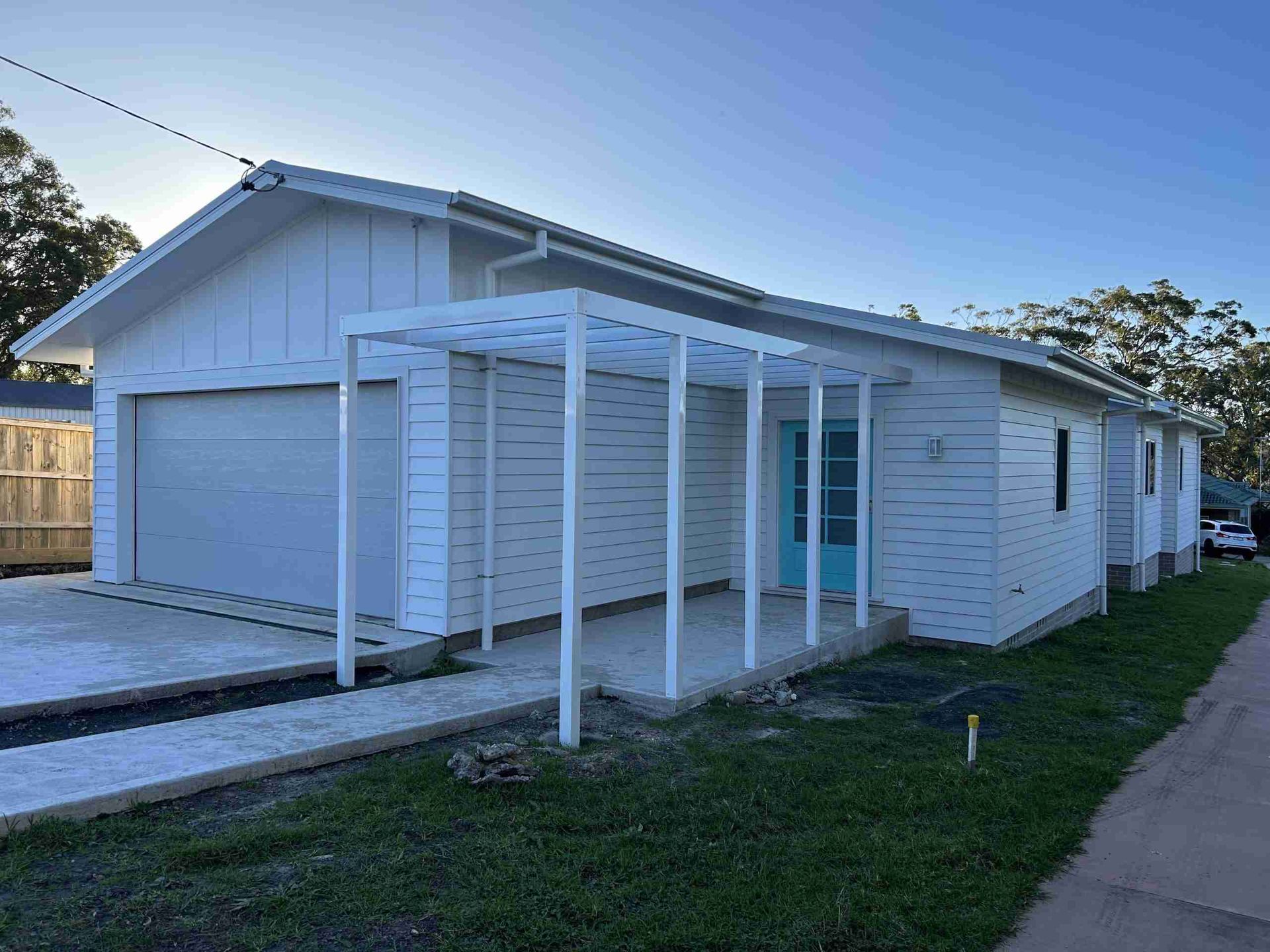 White single-story house with a carport, blue-gray garage door, and a walkway beside a lawn