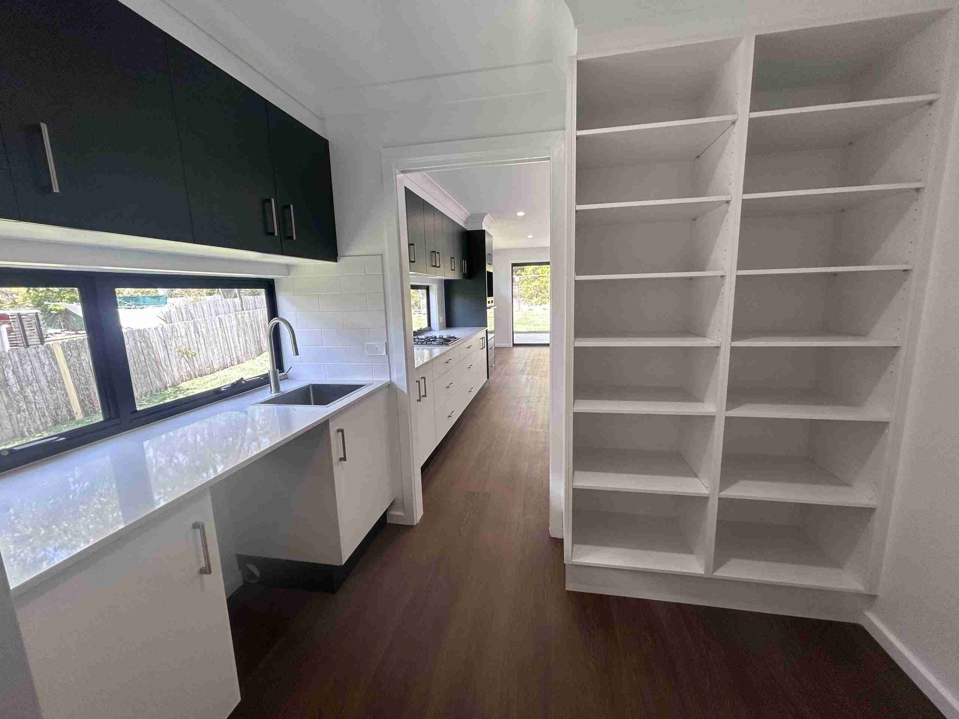 Modern kitchen with white shelves, dark cabinets, and long countertop with sink and window