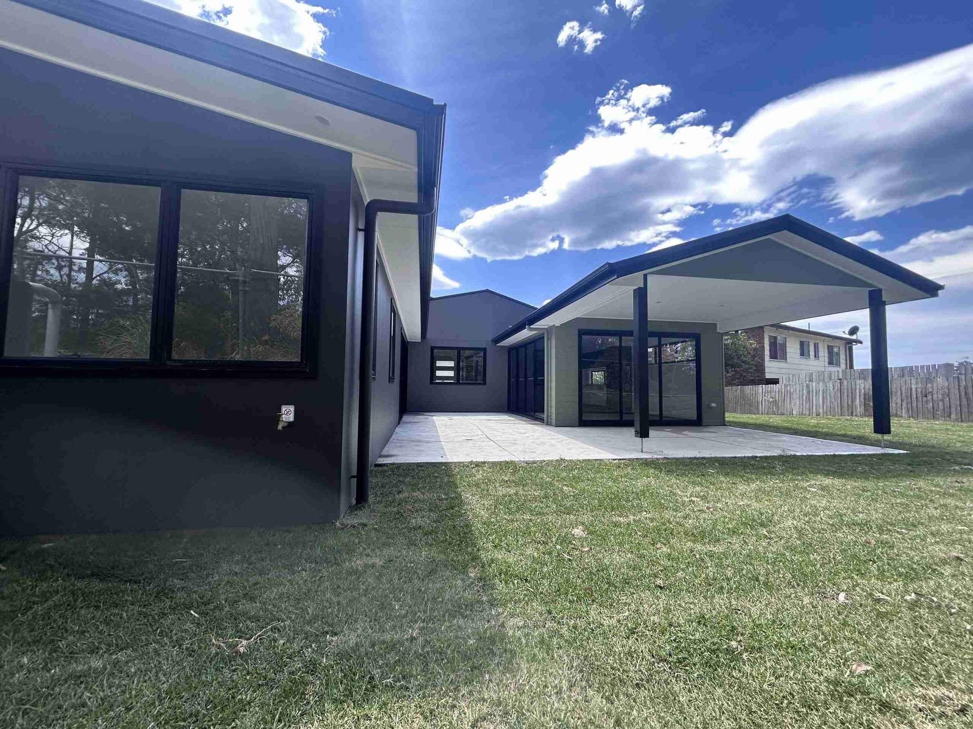 Modern house exterior with black-and-white buildings, a covered patio, and a grassy yard under a blue sky