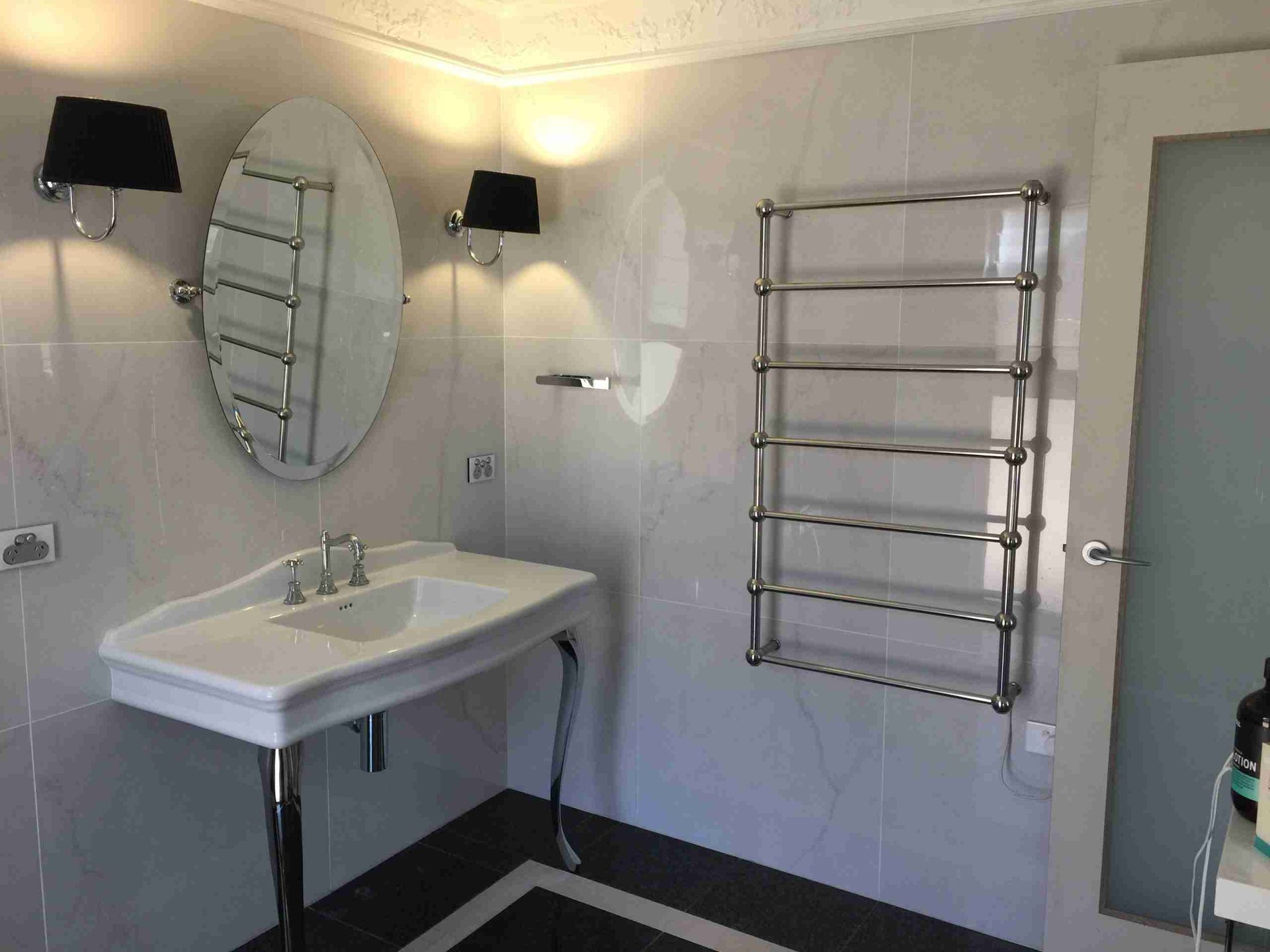 Modern bathroom with sink, oval mirror, towel rack, wall lights, and tiled walls